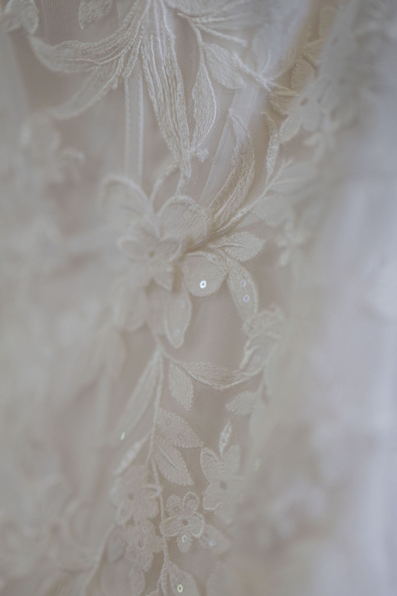 Close-up of elegant white bridal lace fabric with floral embroidery and delicate sequin details.