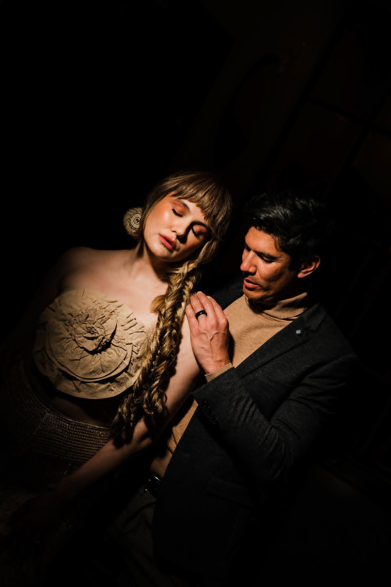 Two performers in dramatic lighting, woman with braided hair in ornate costume, man in dark jacket gazing at her tenderly.