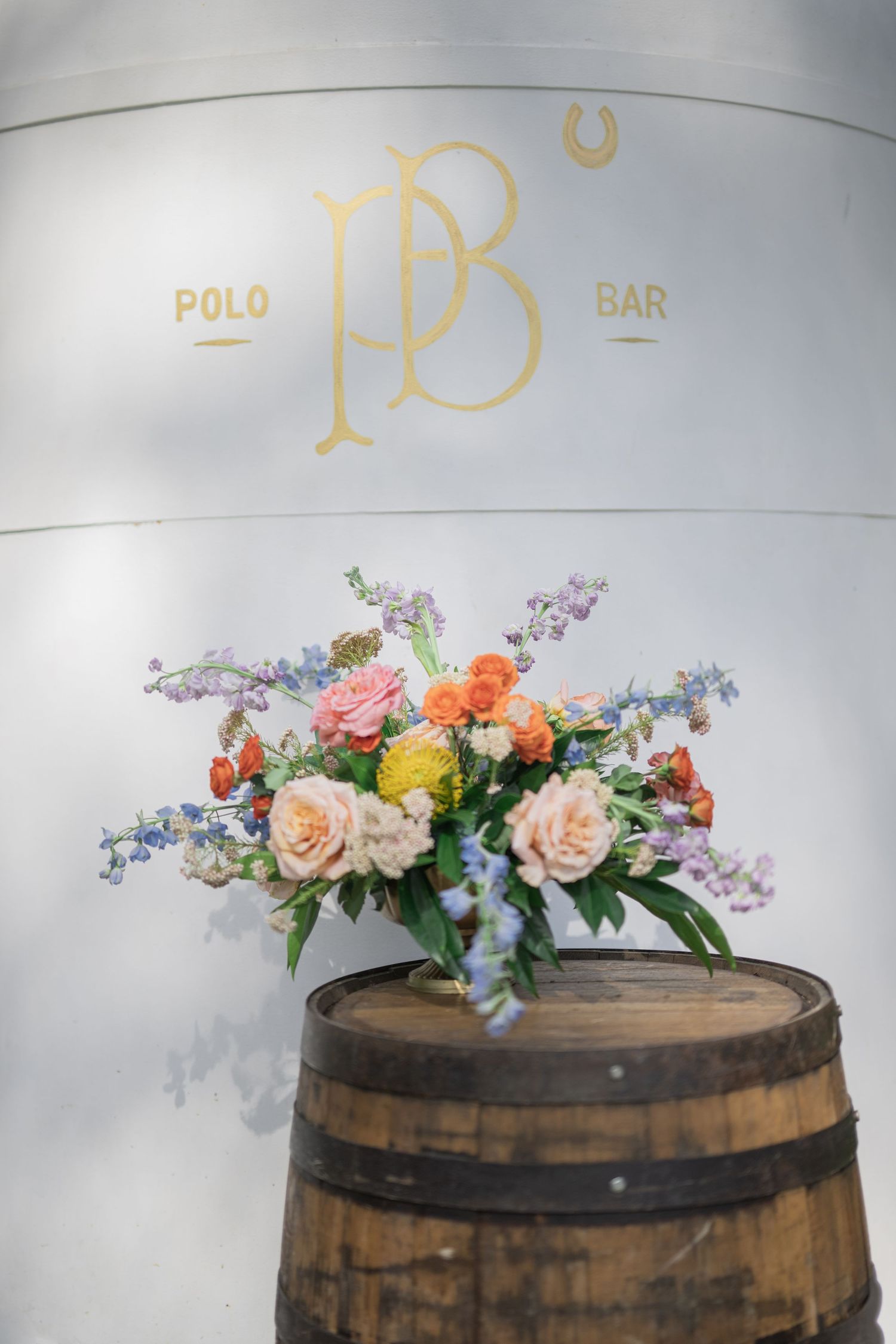 Colorful floral arrangement on a wooden barrel in front of the Polo Bar logo sign.