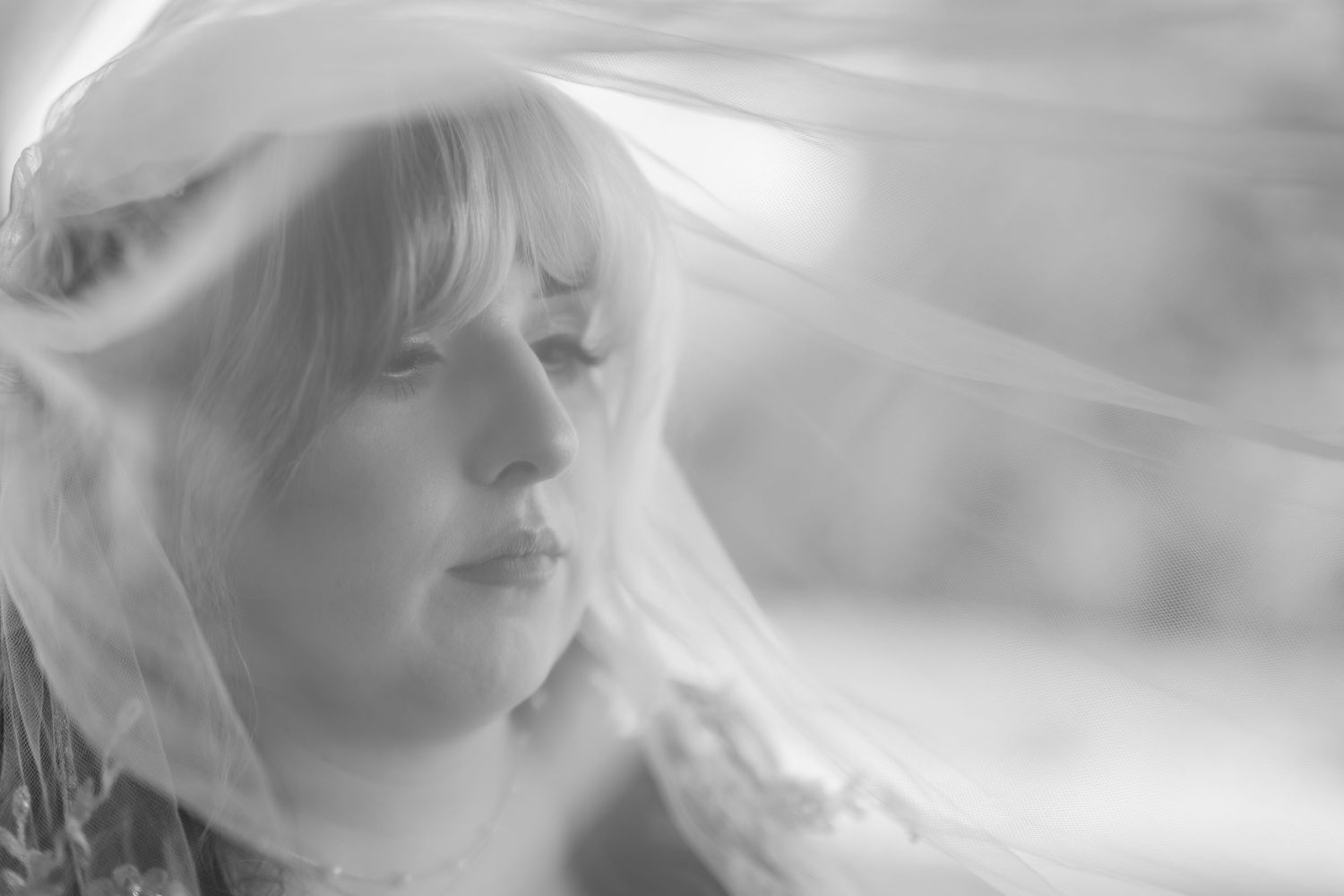 Black and white portrait of a blonde woman draped in a sheer veil, gazing softly to the side.