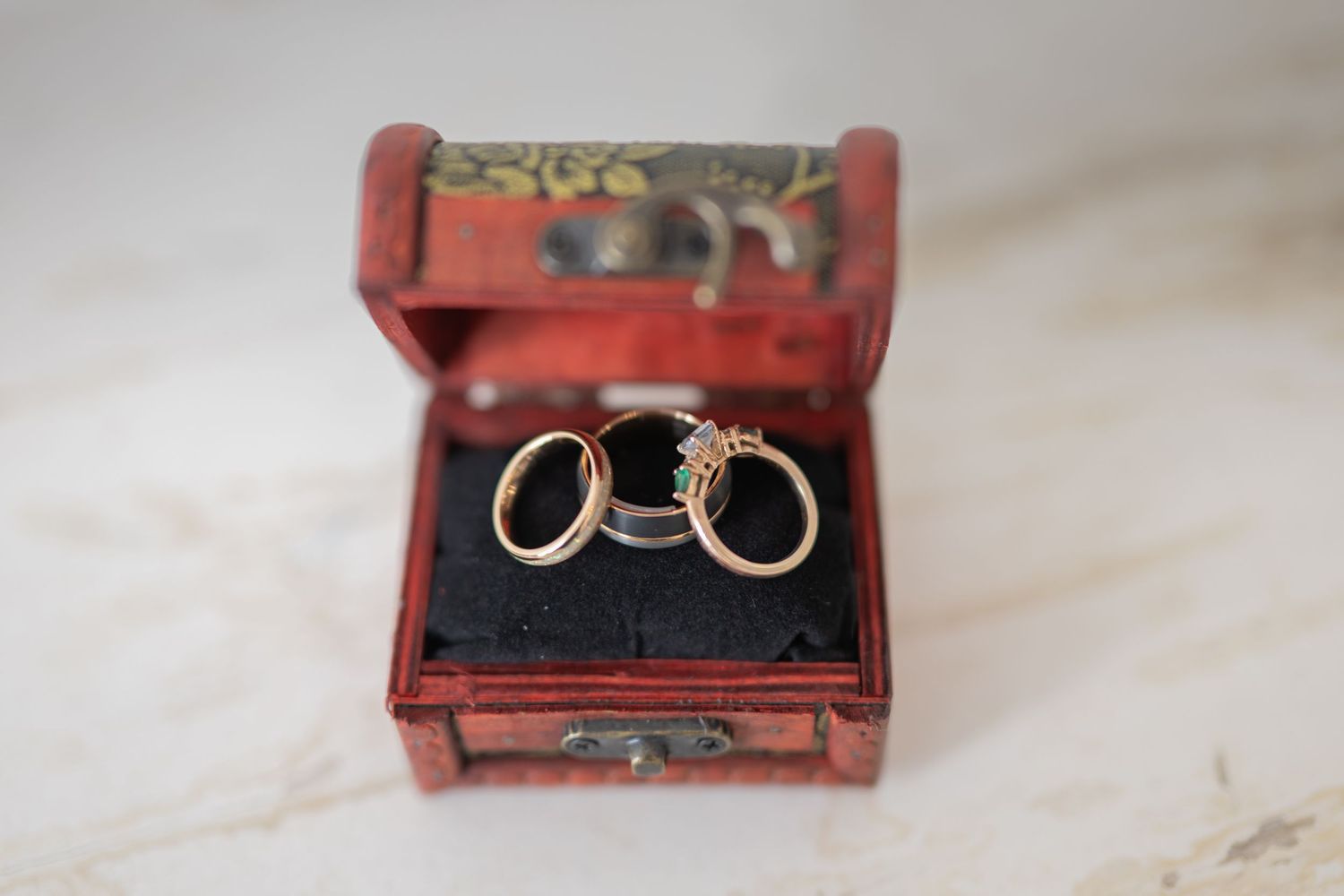 Three gold wedding rings displayed in an ornate red vintage jewelry box on a marble surface.