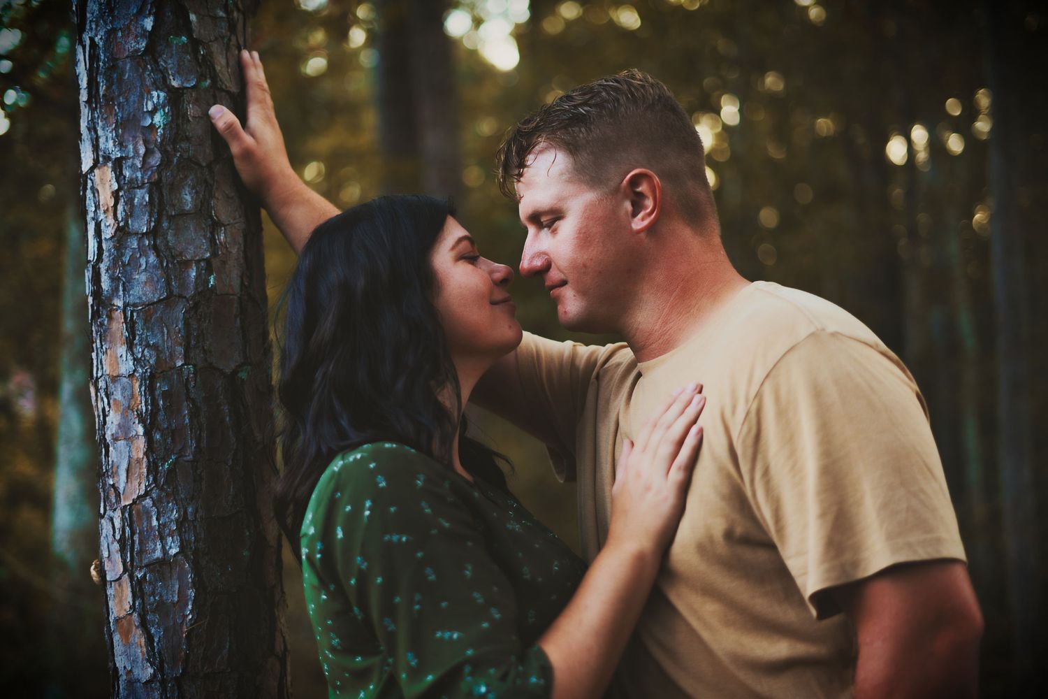 Romantic couple embraces among pine trees during golden hour photo session.