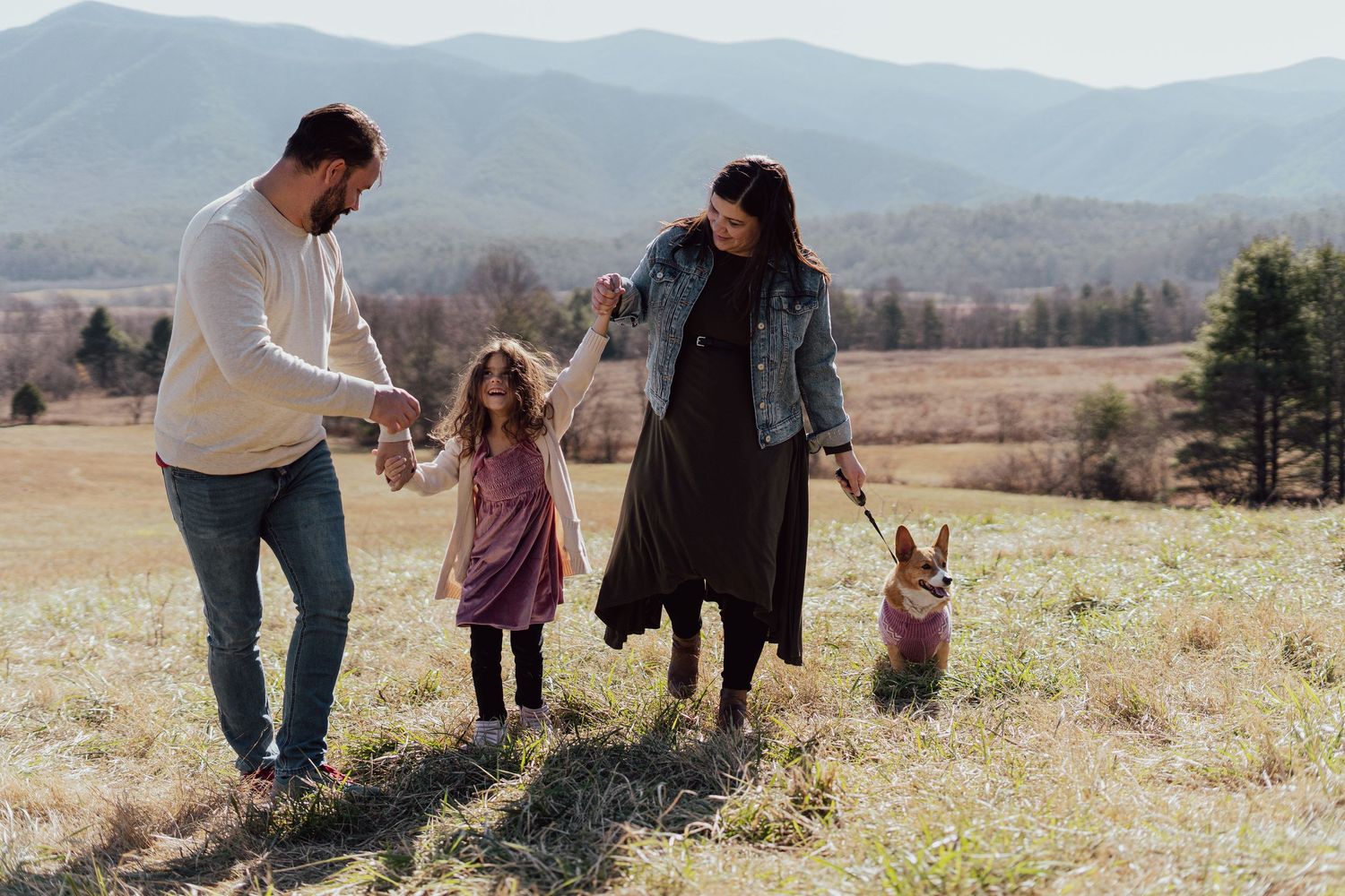 A family walks together through a grassy field with mountains visible in the distance.