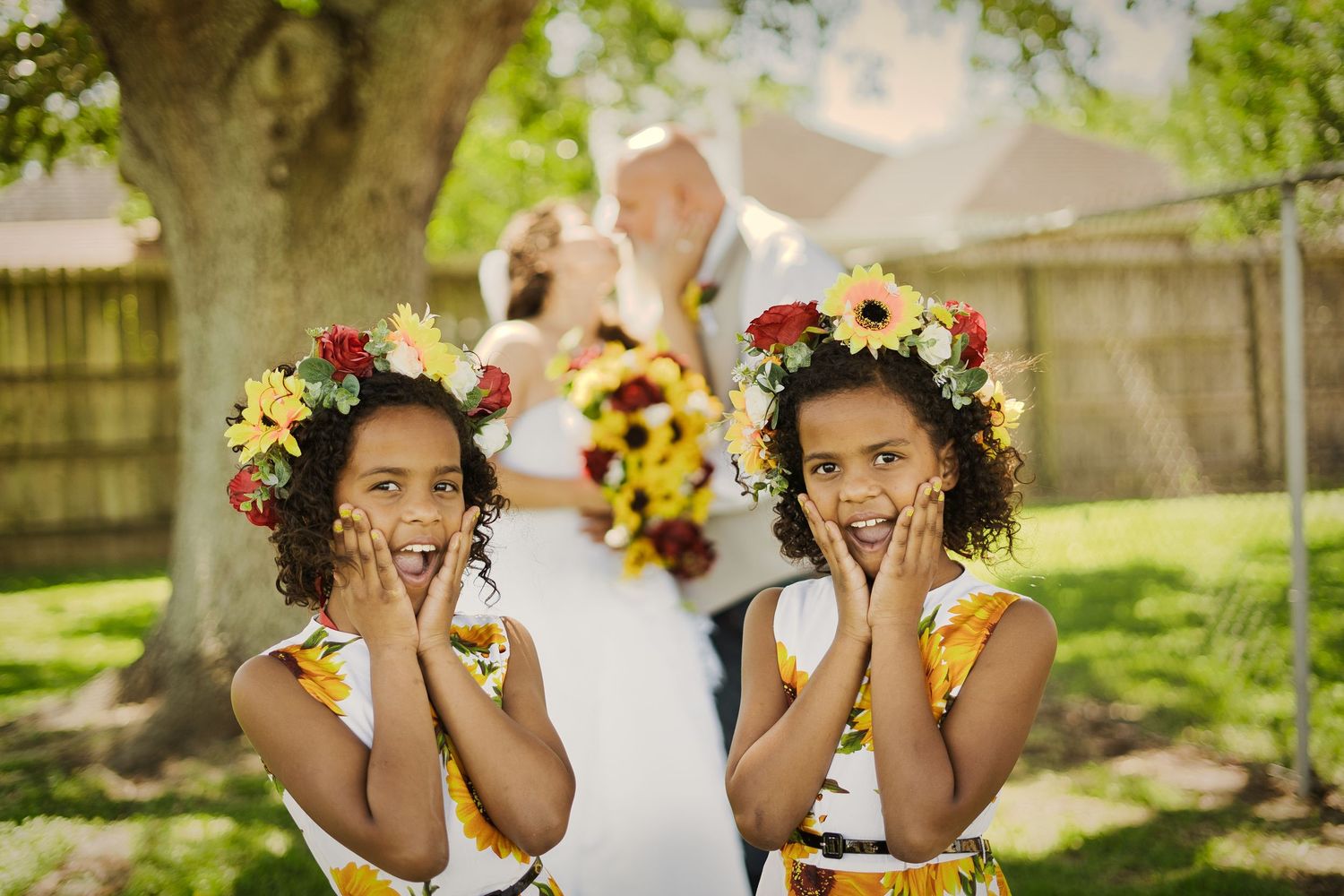 Flower girls wearing sunflower crowns laugh and cover their faces during outdoor photo session.