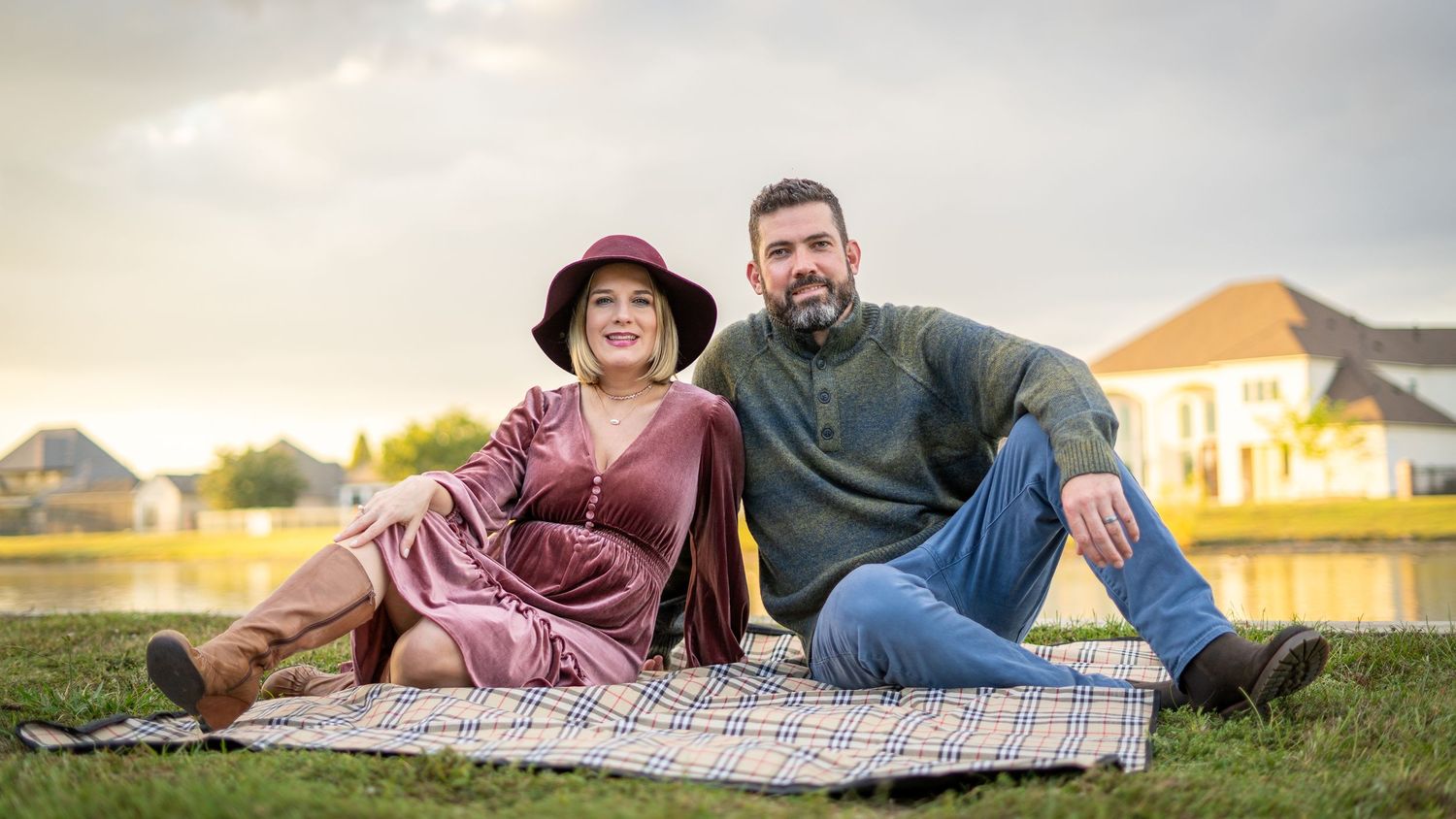 Couple enjoys a picnic on a blanket in a grassy field at sunset.
