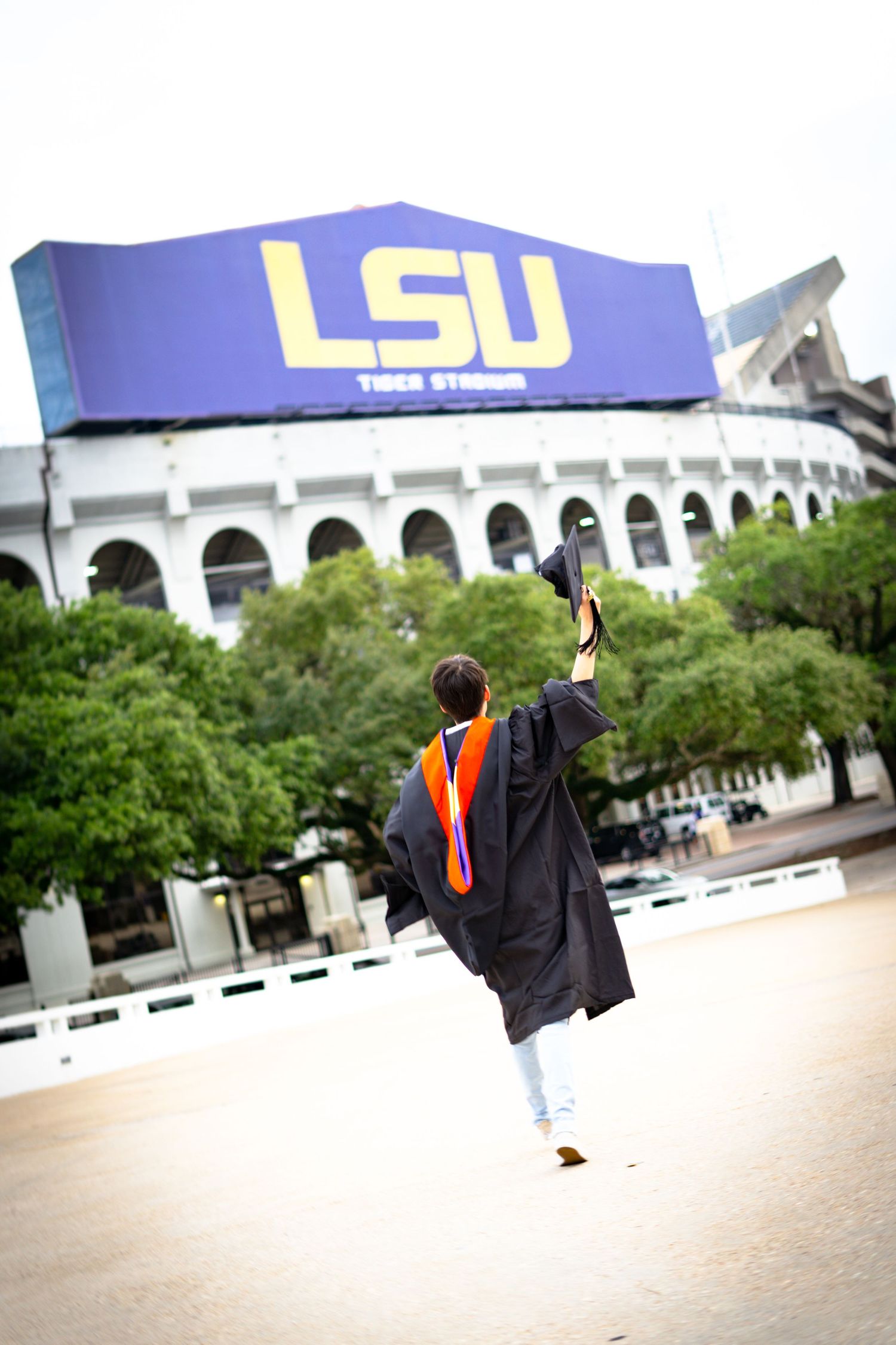 Graduate in cap and gown walks away from LSU stadium during graduation photo session.