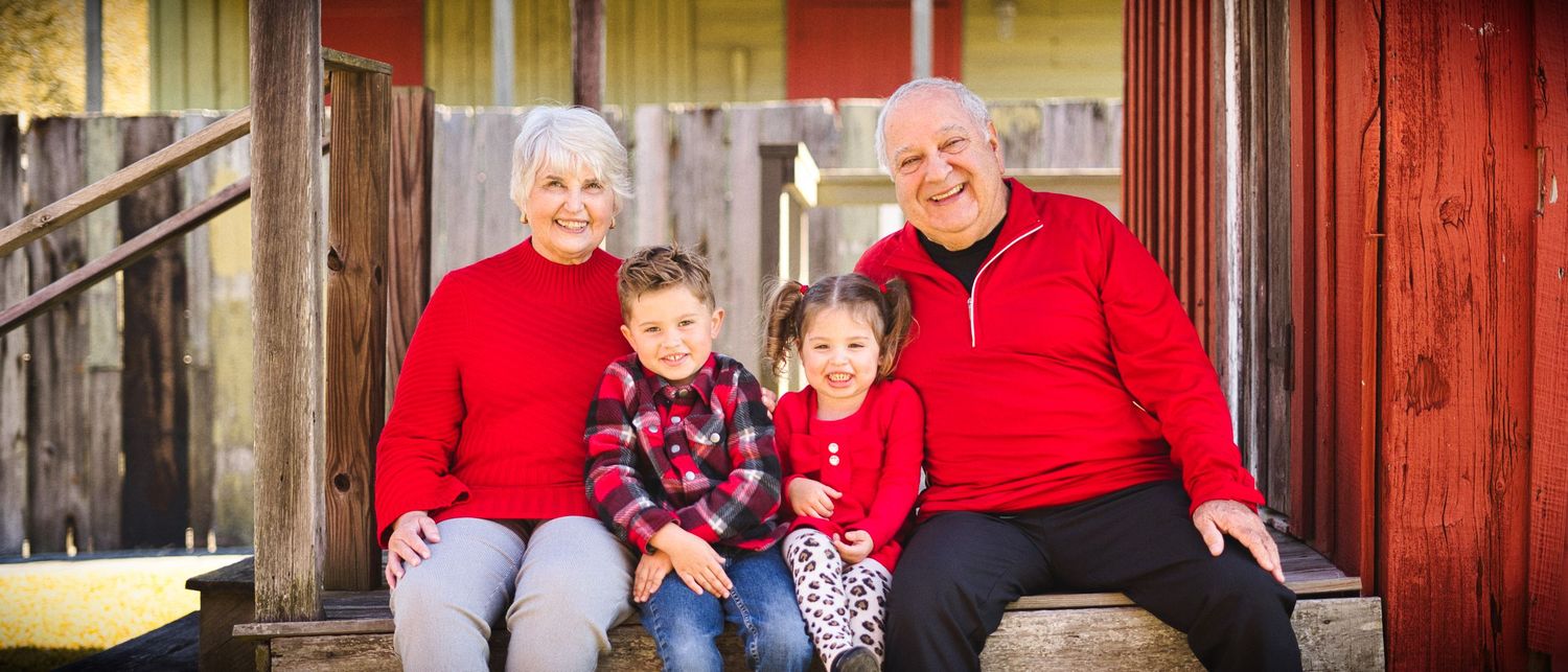 Family wearing coordinated red outfits poses together for holiday portraits against a rustic backdrop.