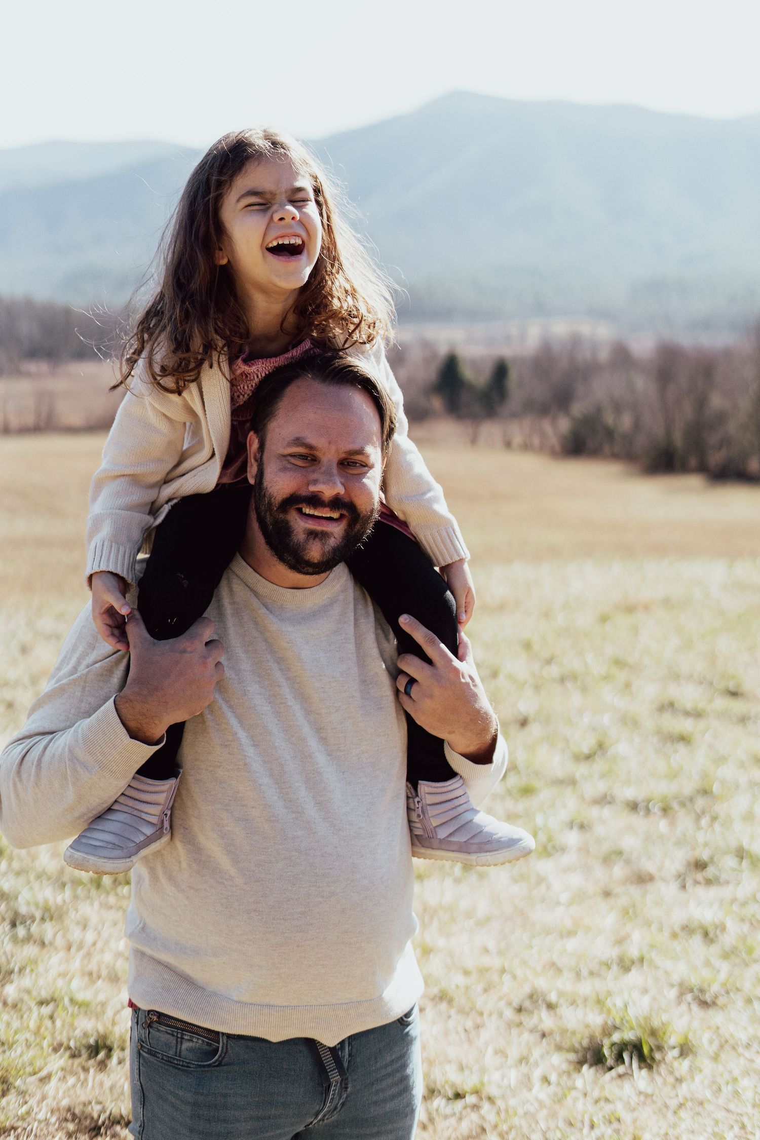 A playful piggyback ride moment captured in a sunny field with mountains in the background.