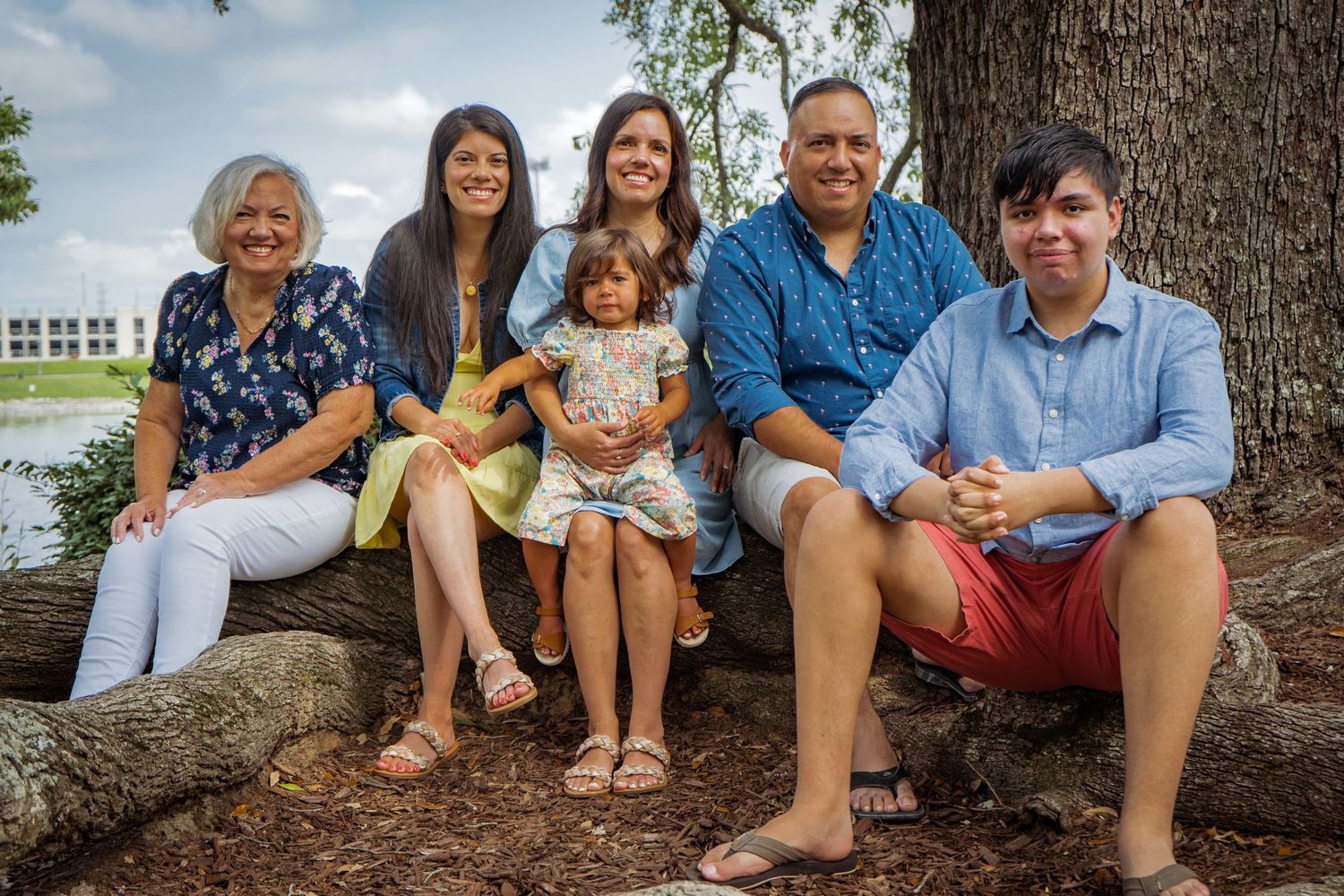 Extended family group sitting casually together on tree roots by water.
