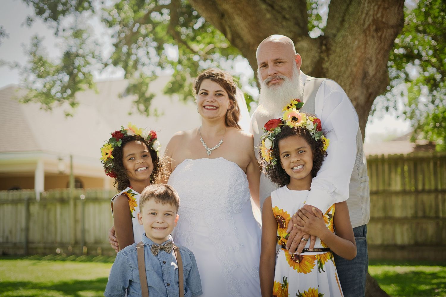 Young flower girls in white dresses with floral crowns pose playfully in a garden setting.
