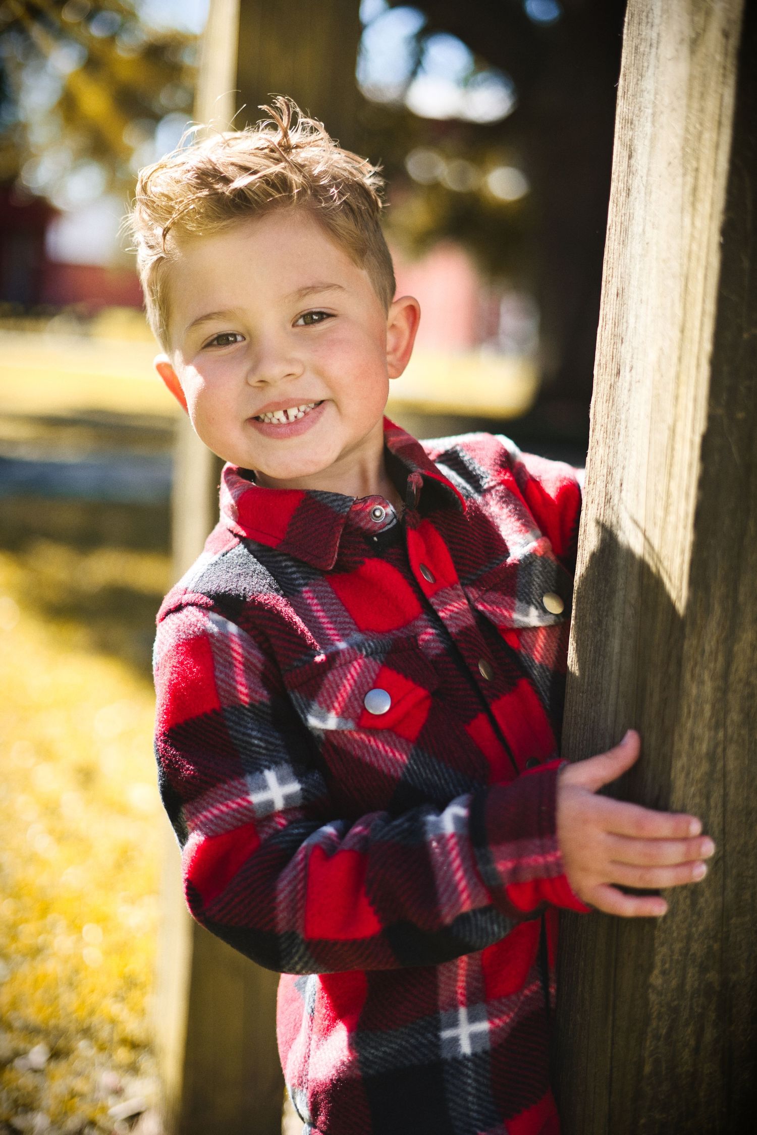Young child in red plaid jacket plays outdoors among autumn leaves.