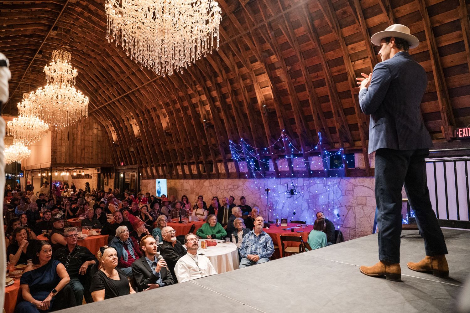 Guests dance and celebrate at an elegant barn wedding reception with crystal chandeliers and rustic wooden beams.
