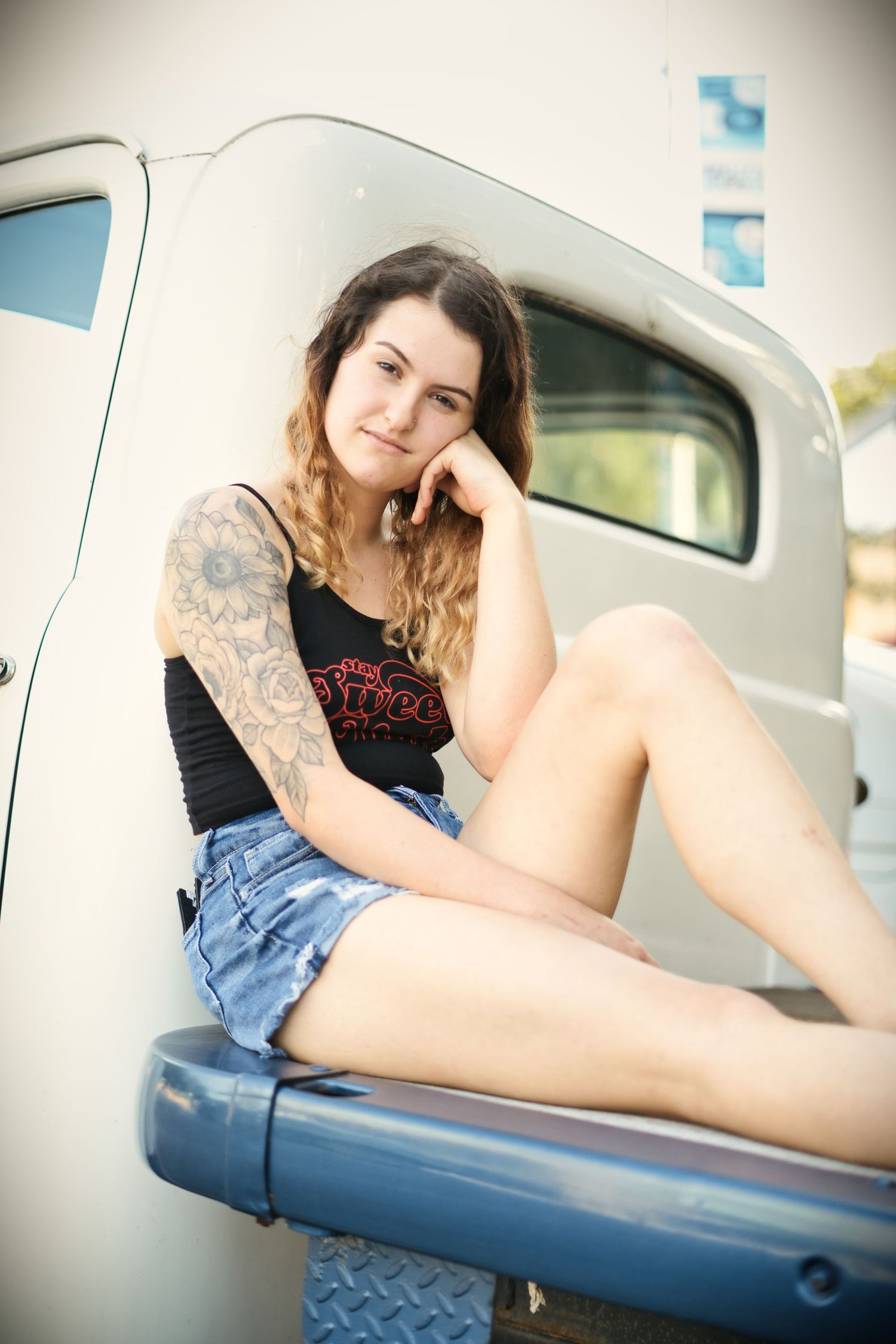 Young woman in denim shorts poses casually on vintage airplane wing.