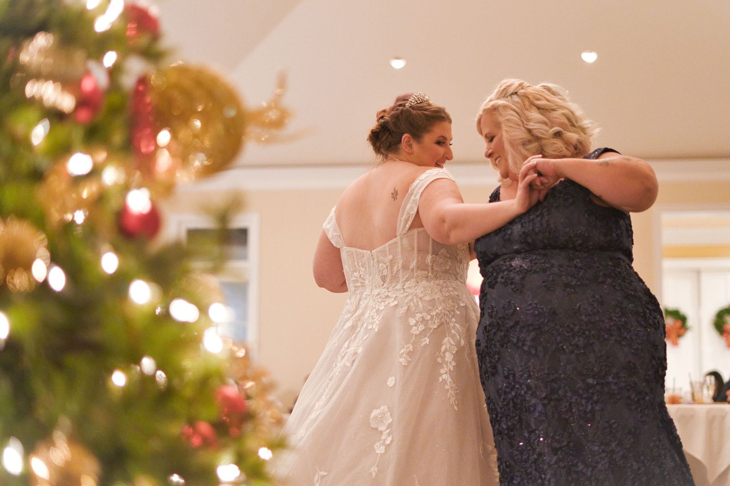 Couples dance together during a formal Christmas wedding reception with decorated trees in background.