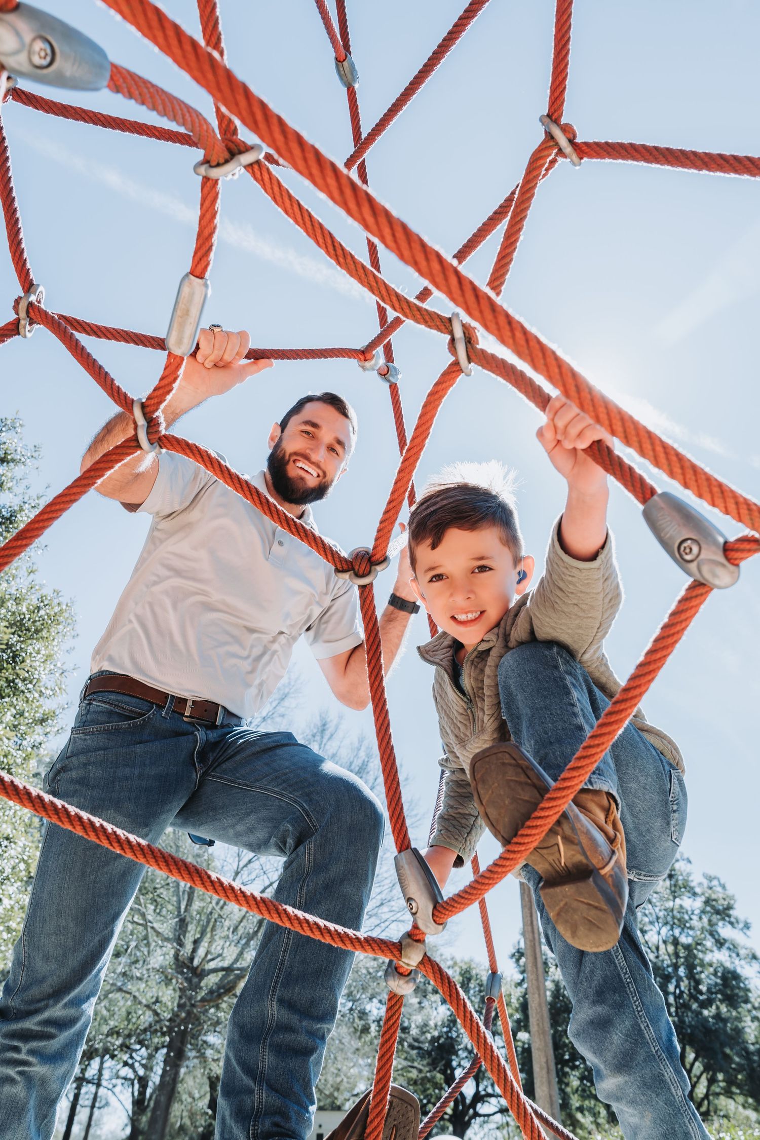 Child playing and climbing on orange rope playground equipment against blue sky.