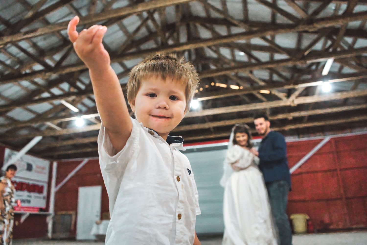 A child raises their arms in celebration inside a rustic barn with exposed wooden beams.