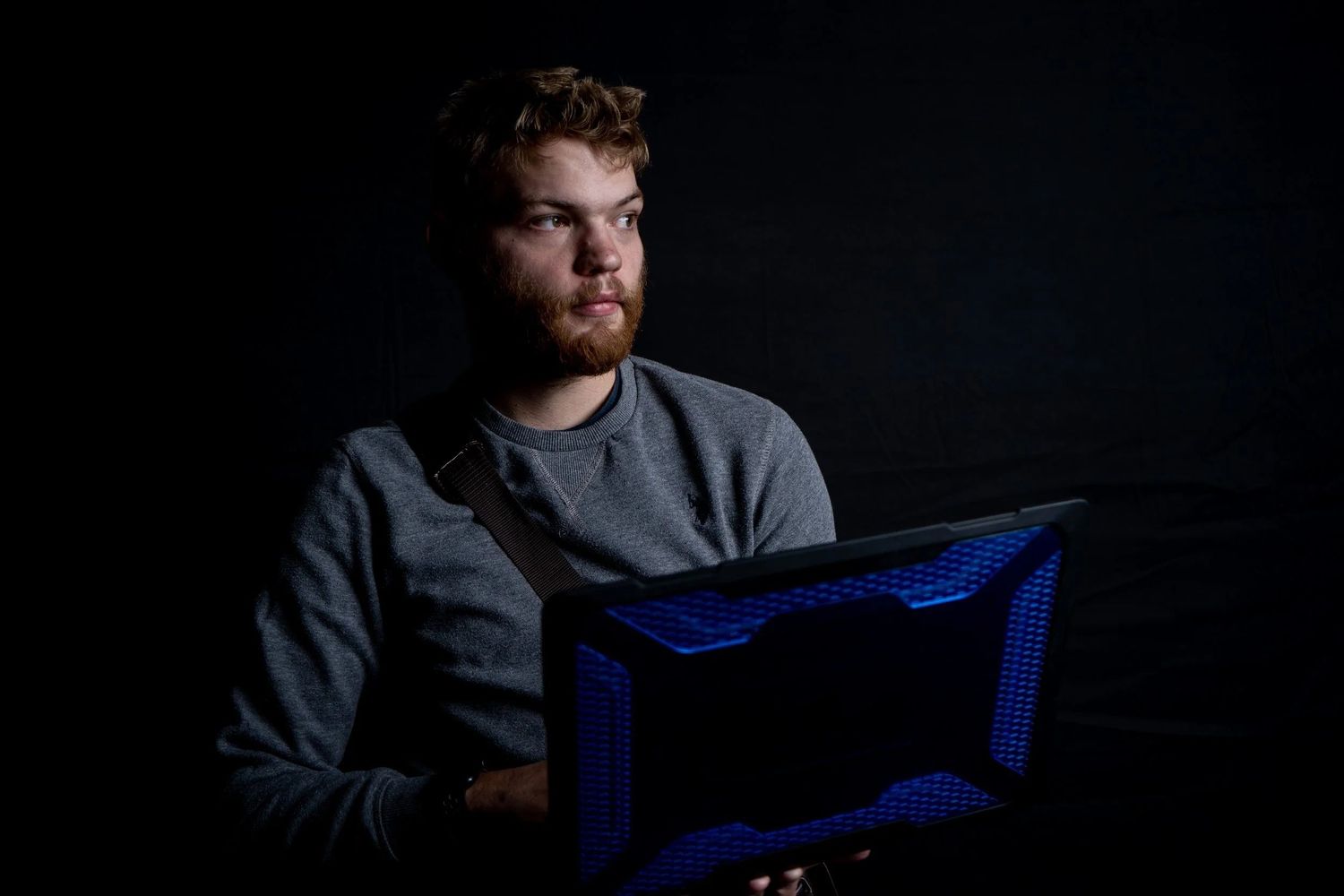 Person in dark room illuminated by blue light from computer screen while working at night.