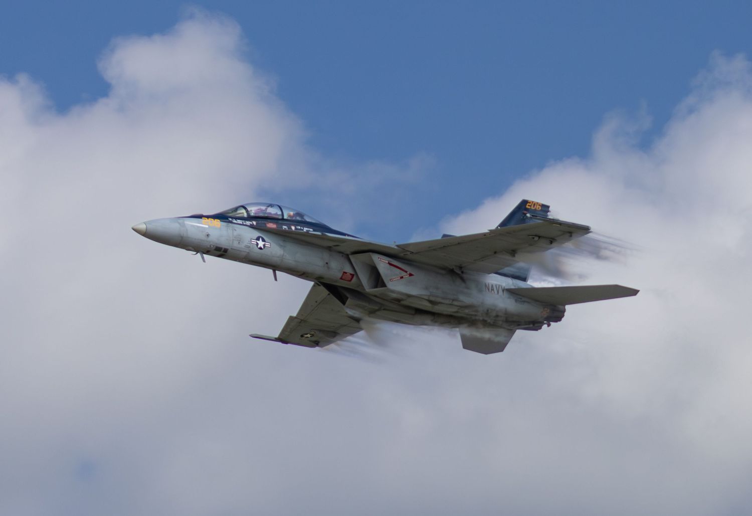 F-18 side view flying with vapor behind the wings