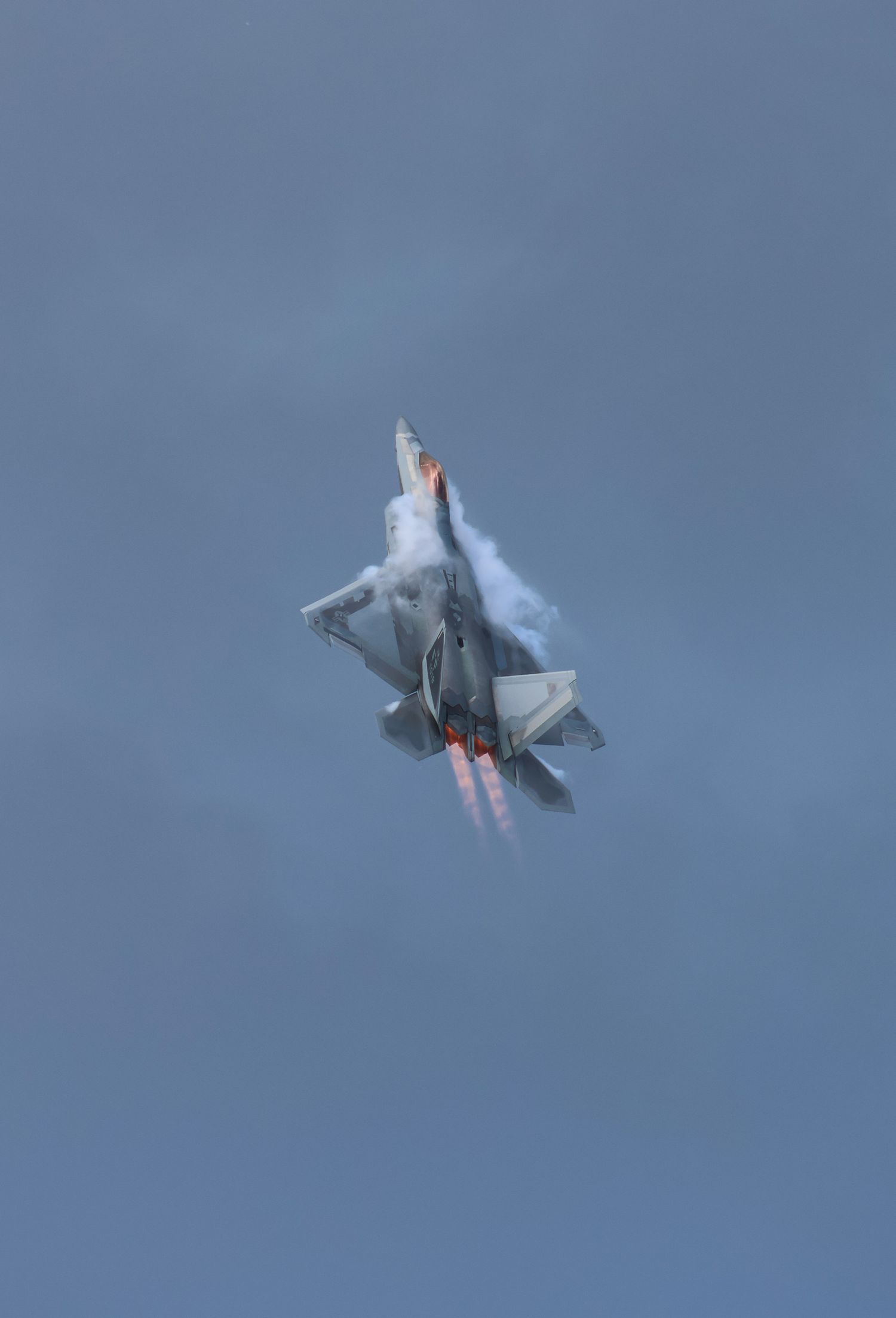 F-22 Raptor flying vertical with afterburners and vapor around the fuselage