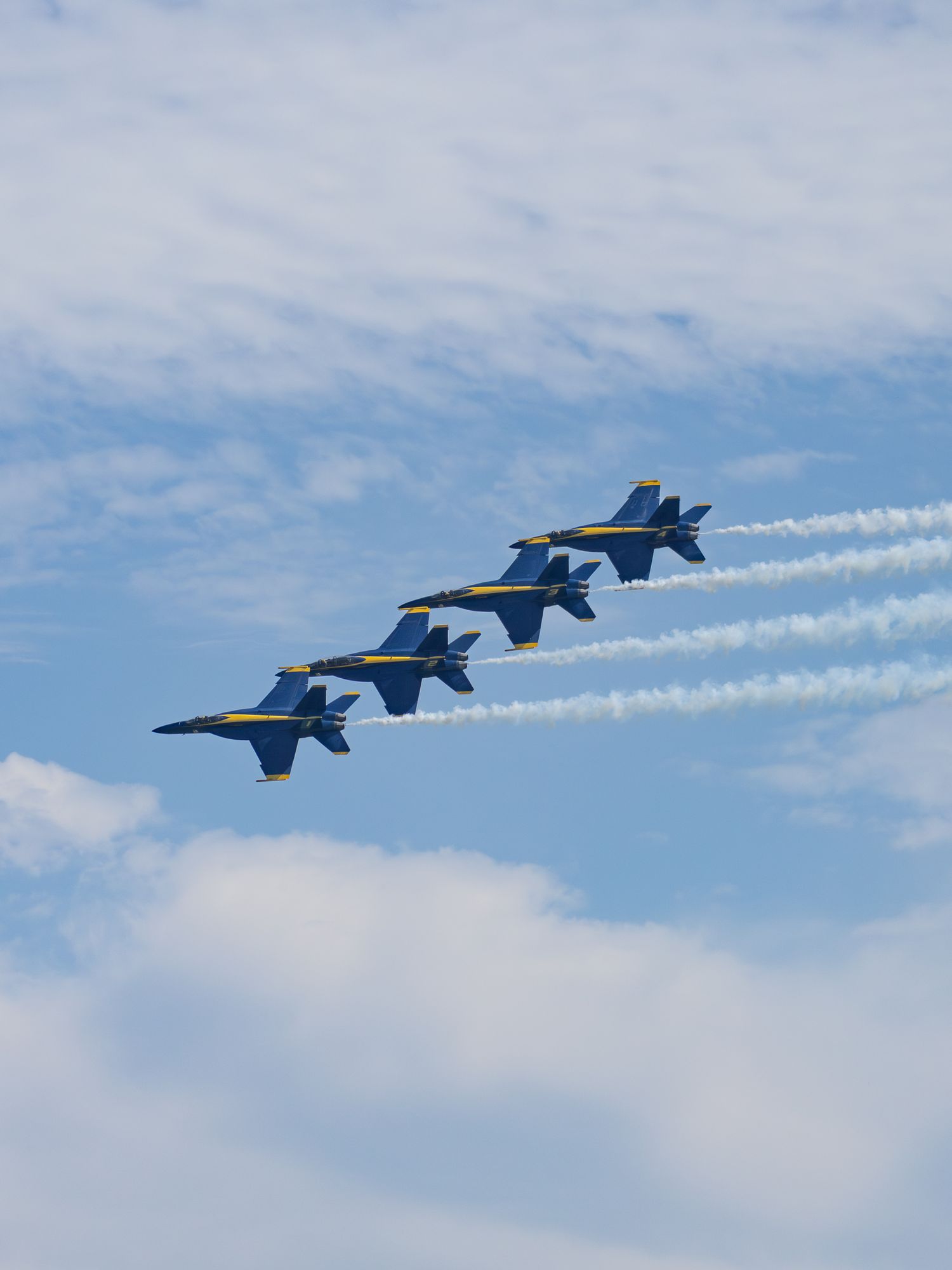 Four F-18 Blue Angels flying in formation with white smoke trails
