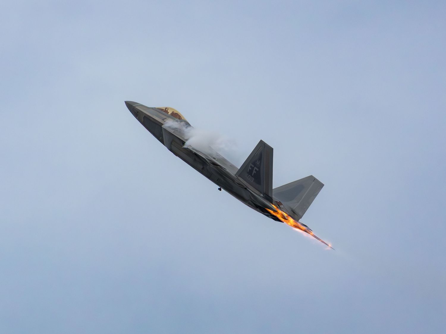 F-22 flying with afterburner and vapor around the wings