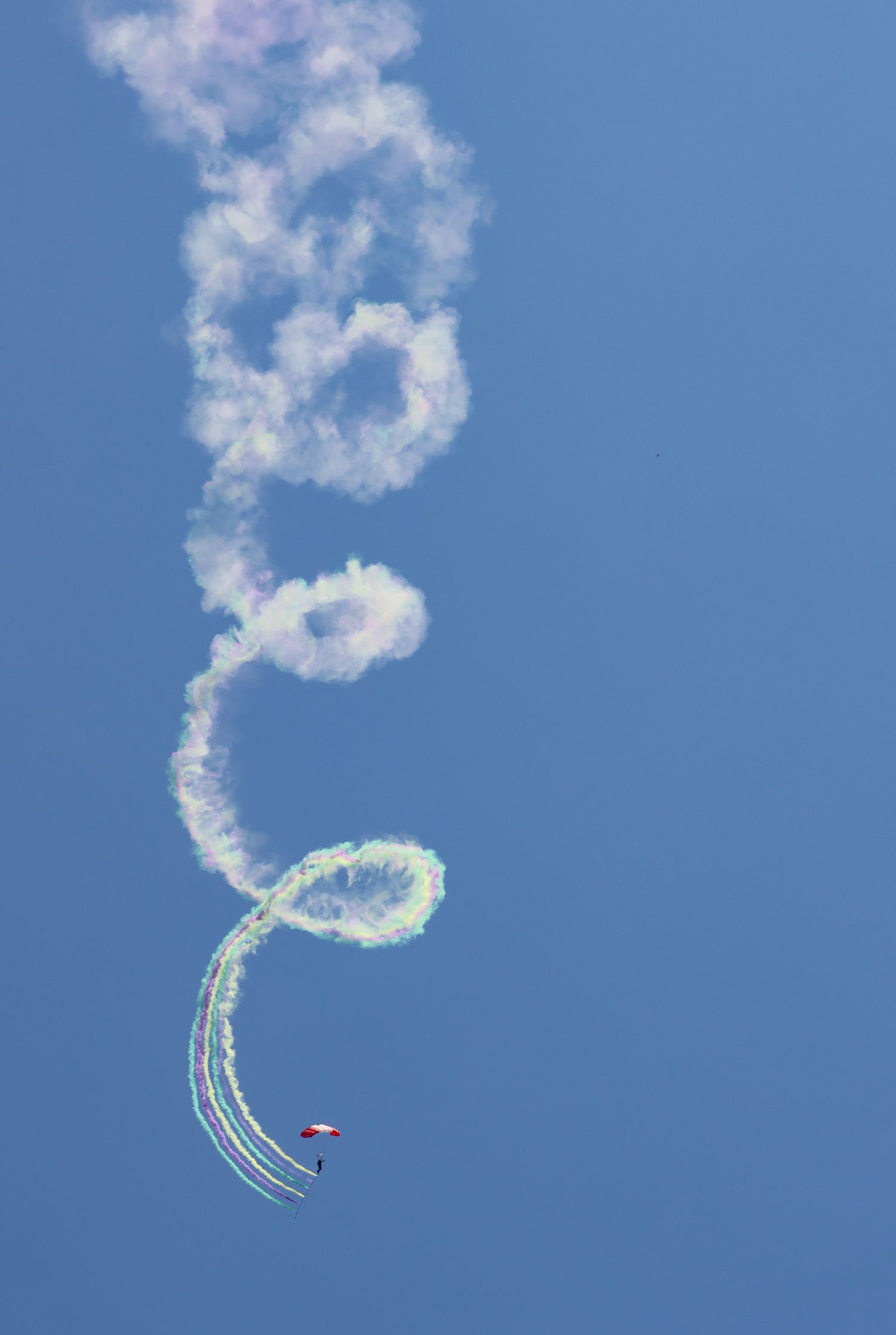 Skydiver flying with parachute and colored smoke trails