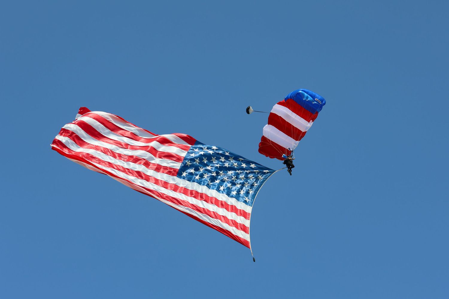 Skydiver diving with red, white, and blue parachute and American flag attached to their foot