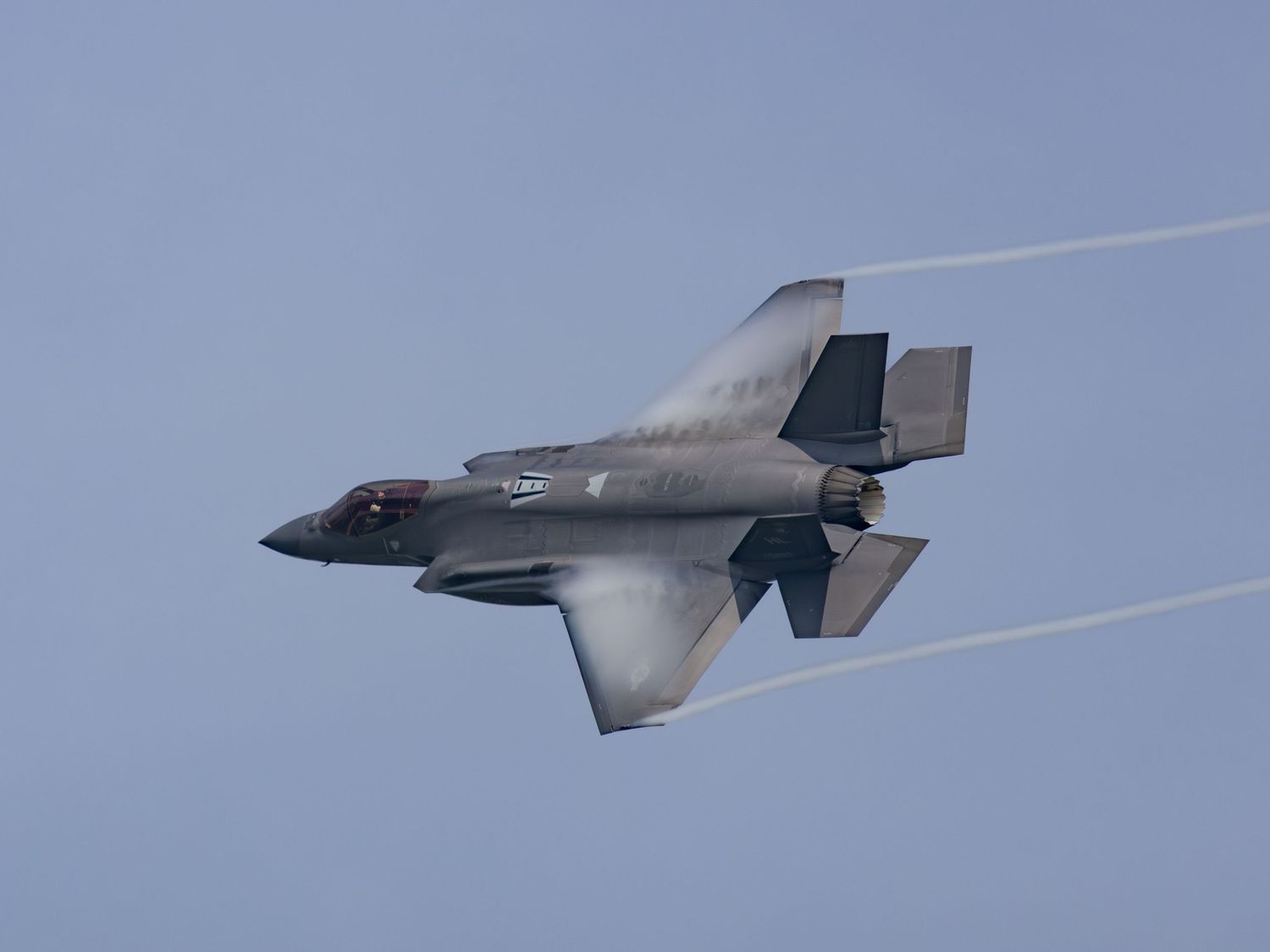 F-35 Lightning flying with vapor around wings and trails off of wing tips