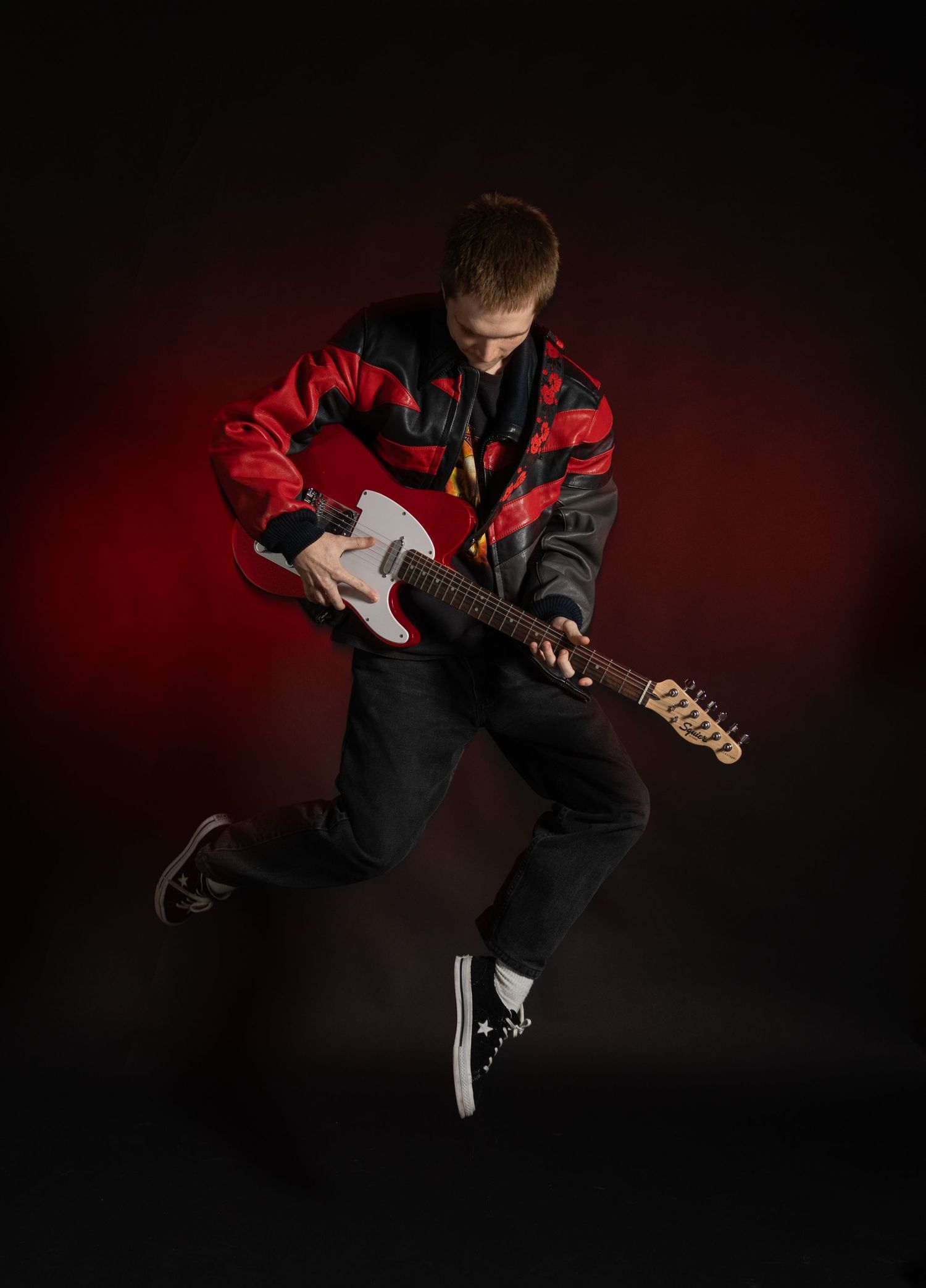 Male model jumping with red guitar in front of red ombre background