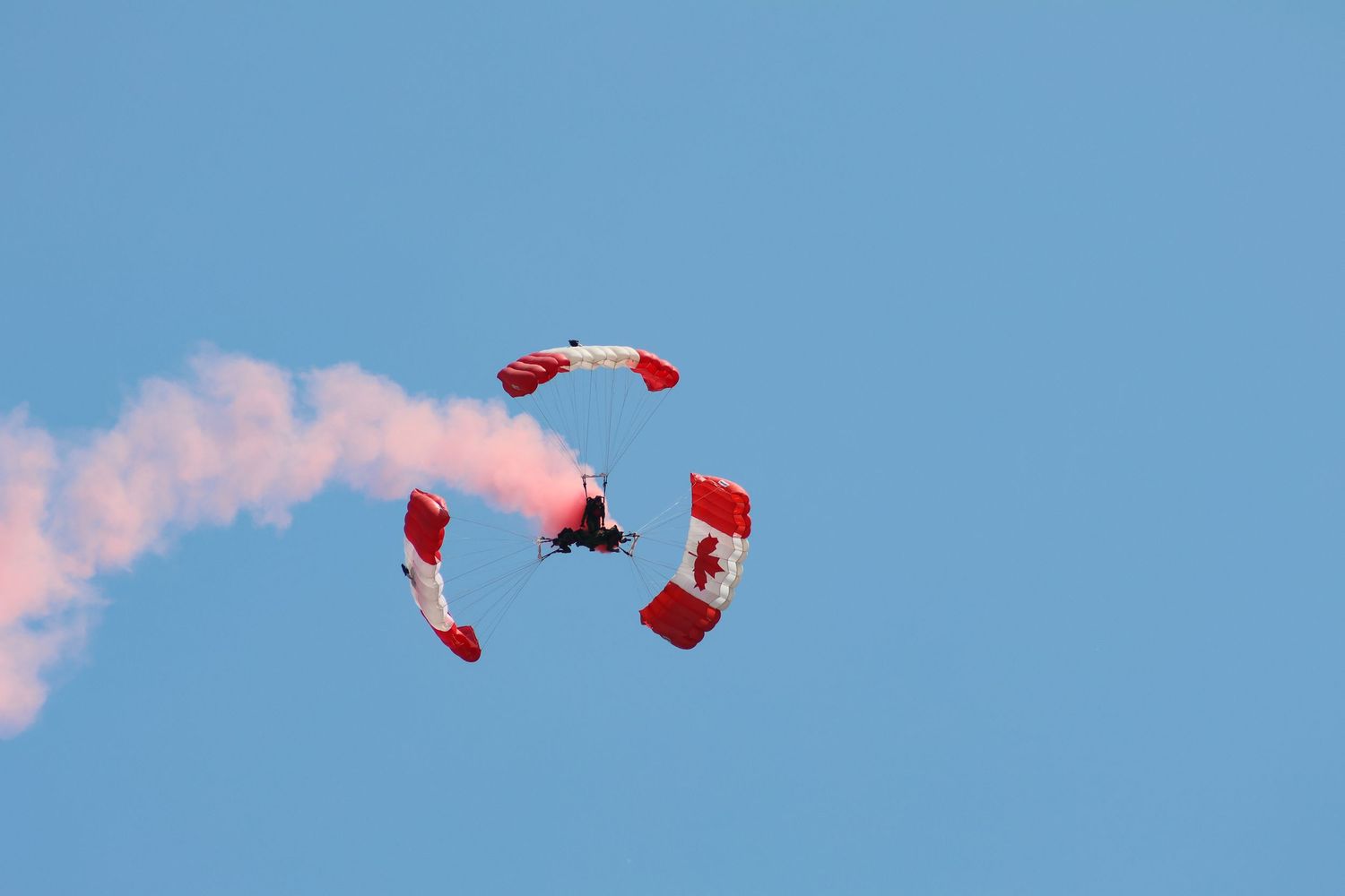 Three skydivers diving together with red smoke and Canadian flag parachutes