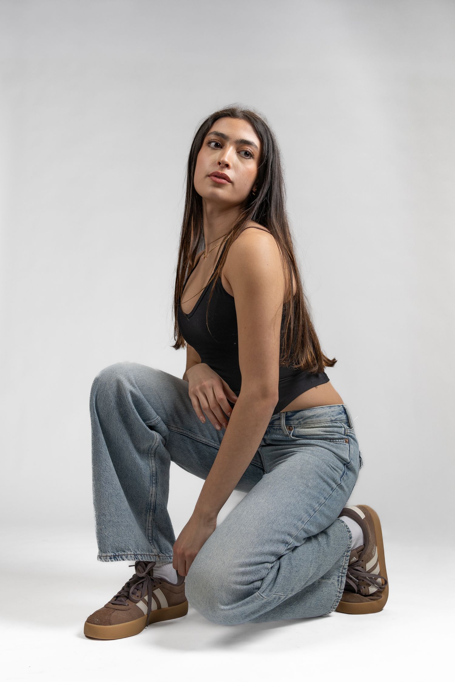 Female model posed crouched on the ground in front of white seamless background