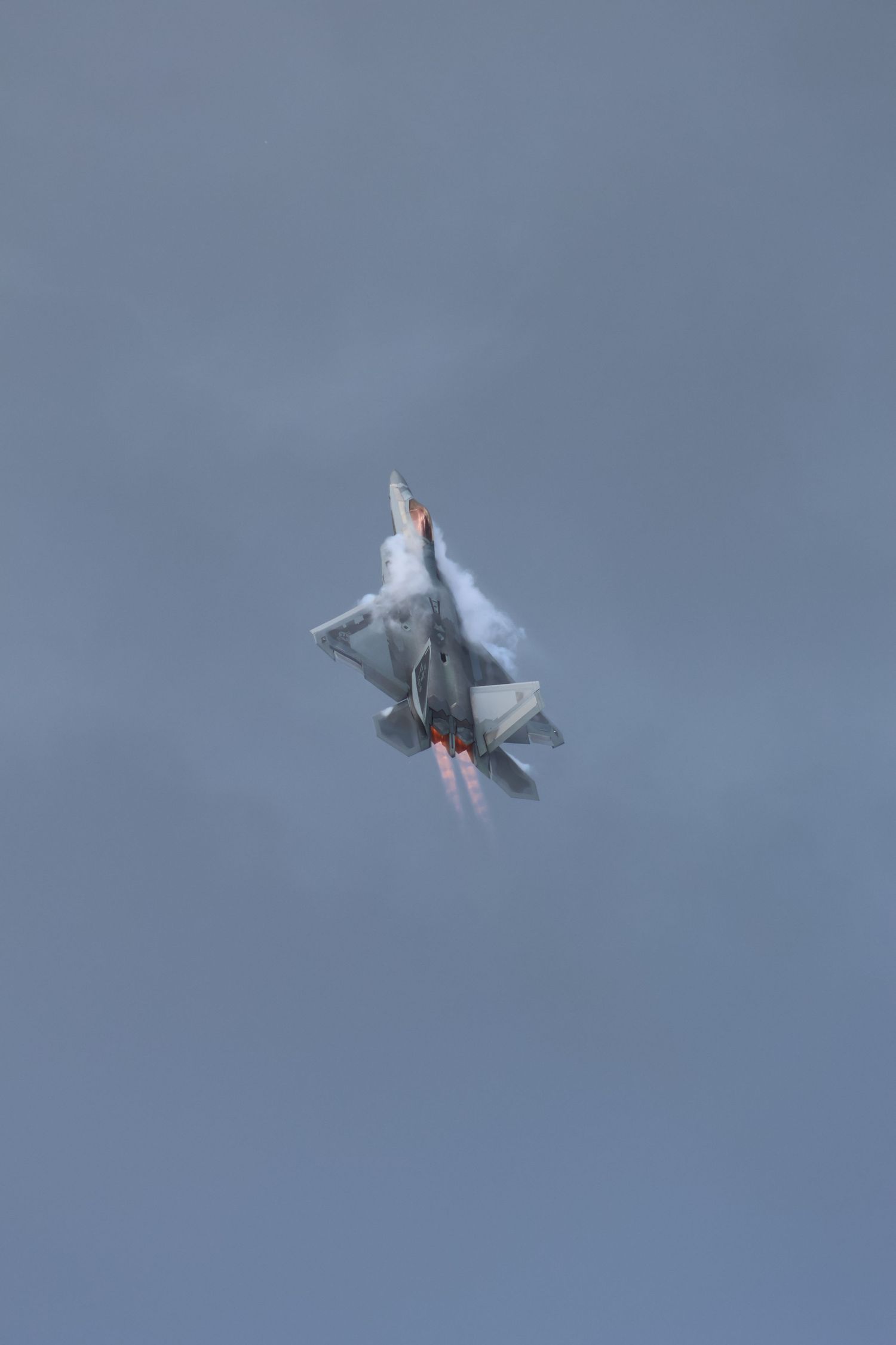 F-22 Raptor flying vertical with afterburners and vapor around the fuselage