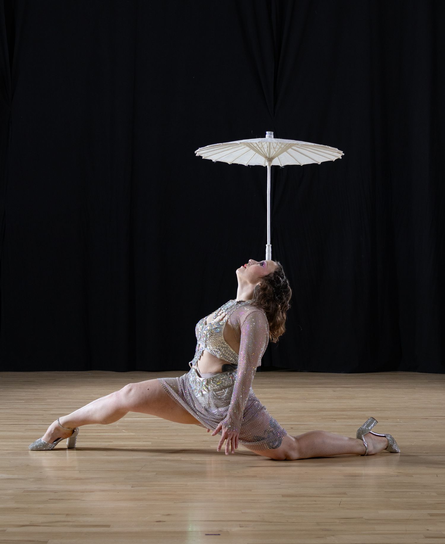 Female model balancing umbrella on forehead in front of black background
