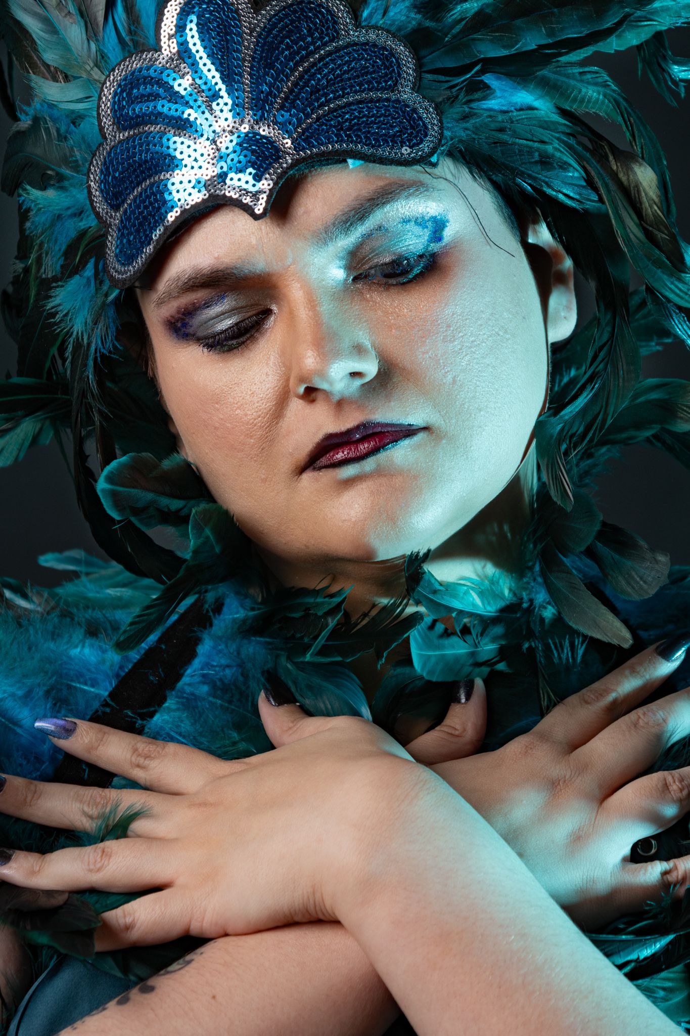 Model with teal feather headdress in front of black background with teal accent lighting