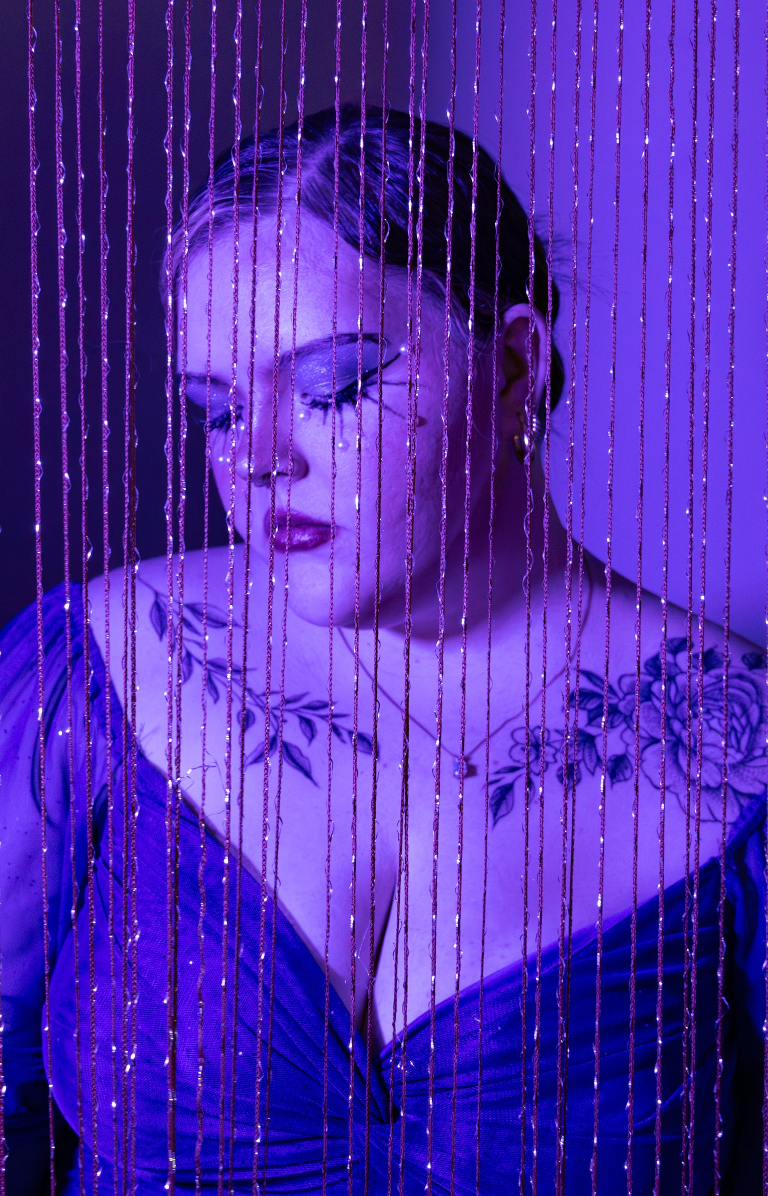 Female model portrait in purple light behind string beads