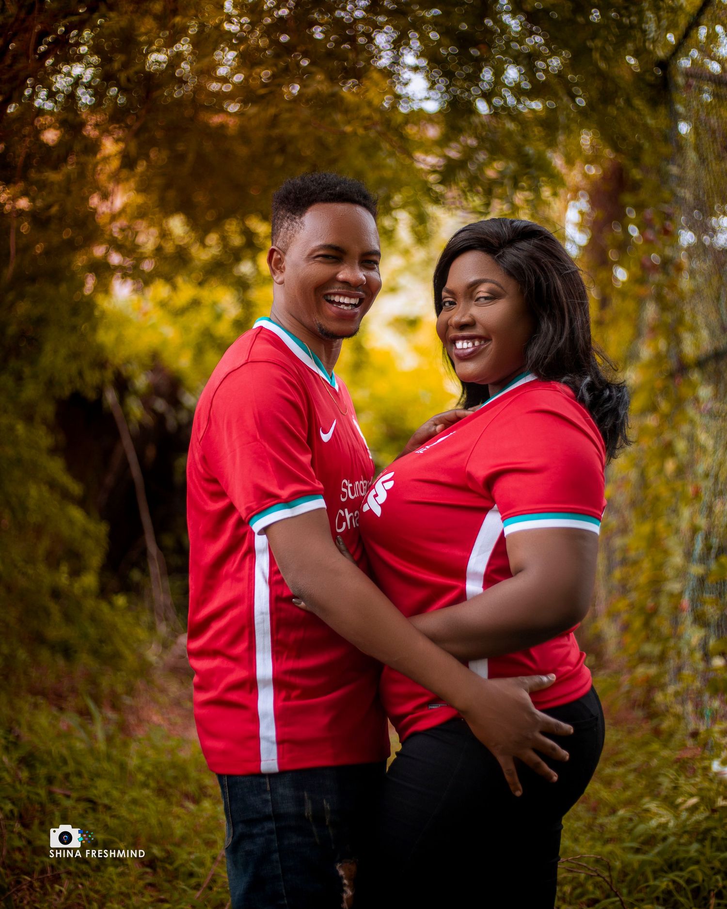 A couple wearing matching red jerseys share loving embraces during an autumn outdoor photoshoot.