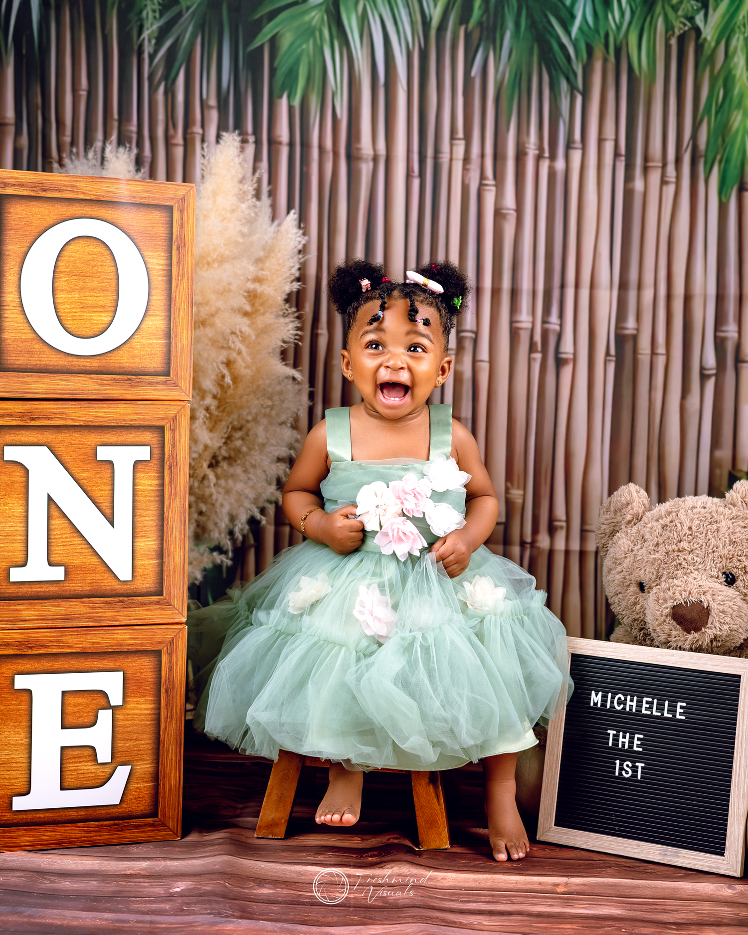 First birthday photoshoot with mint green tutu dress and wooden letter blocks against bamboo backdrop.