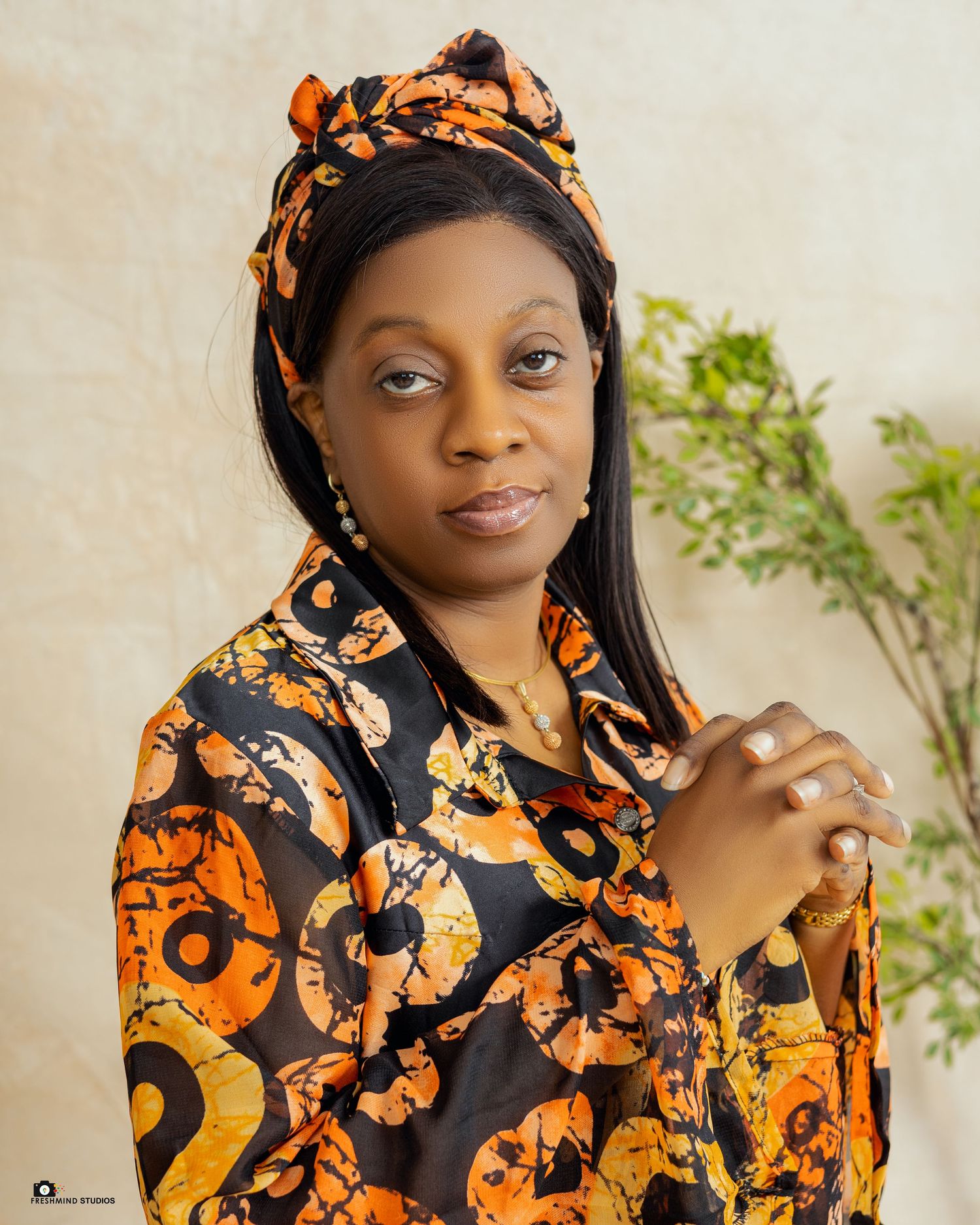 Professional portrait of someone wearing a vibrant orange and black patterned headwrap and matching outfit against a light backdrop.
