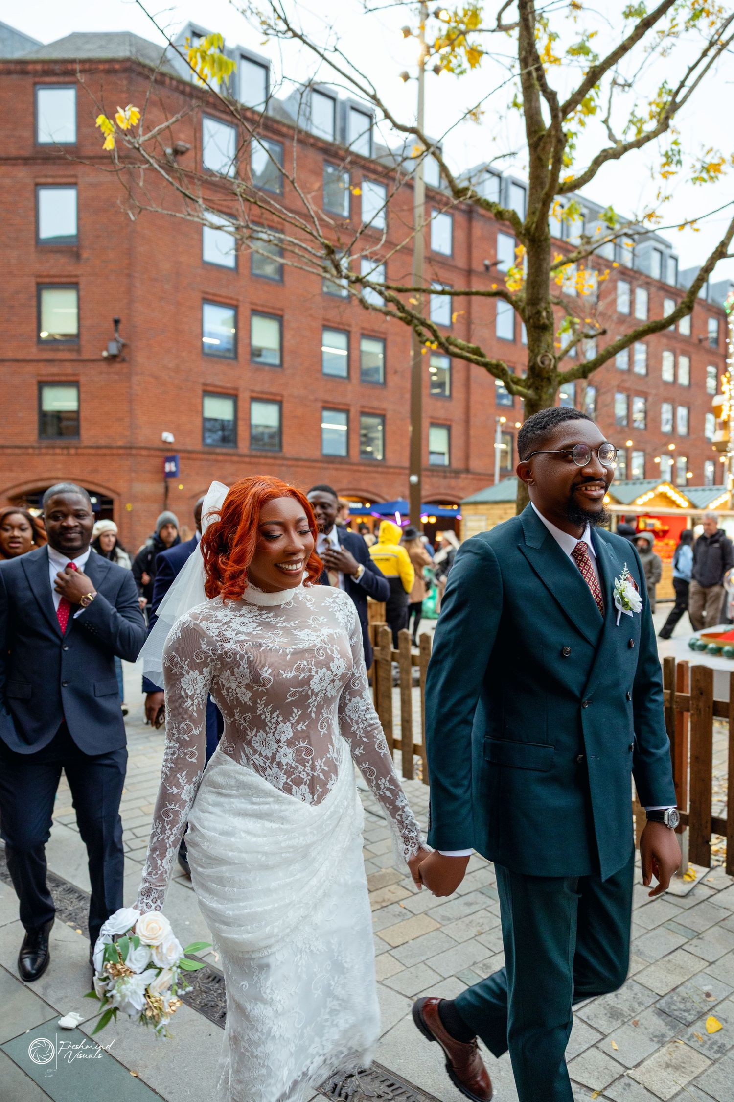 A couple walks together on their wedding day, with the bride wearing a white lace gown and holding a bouquet.