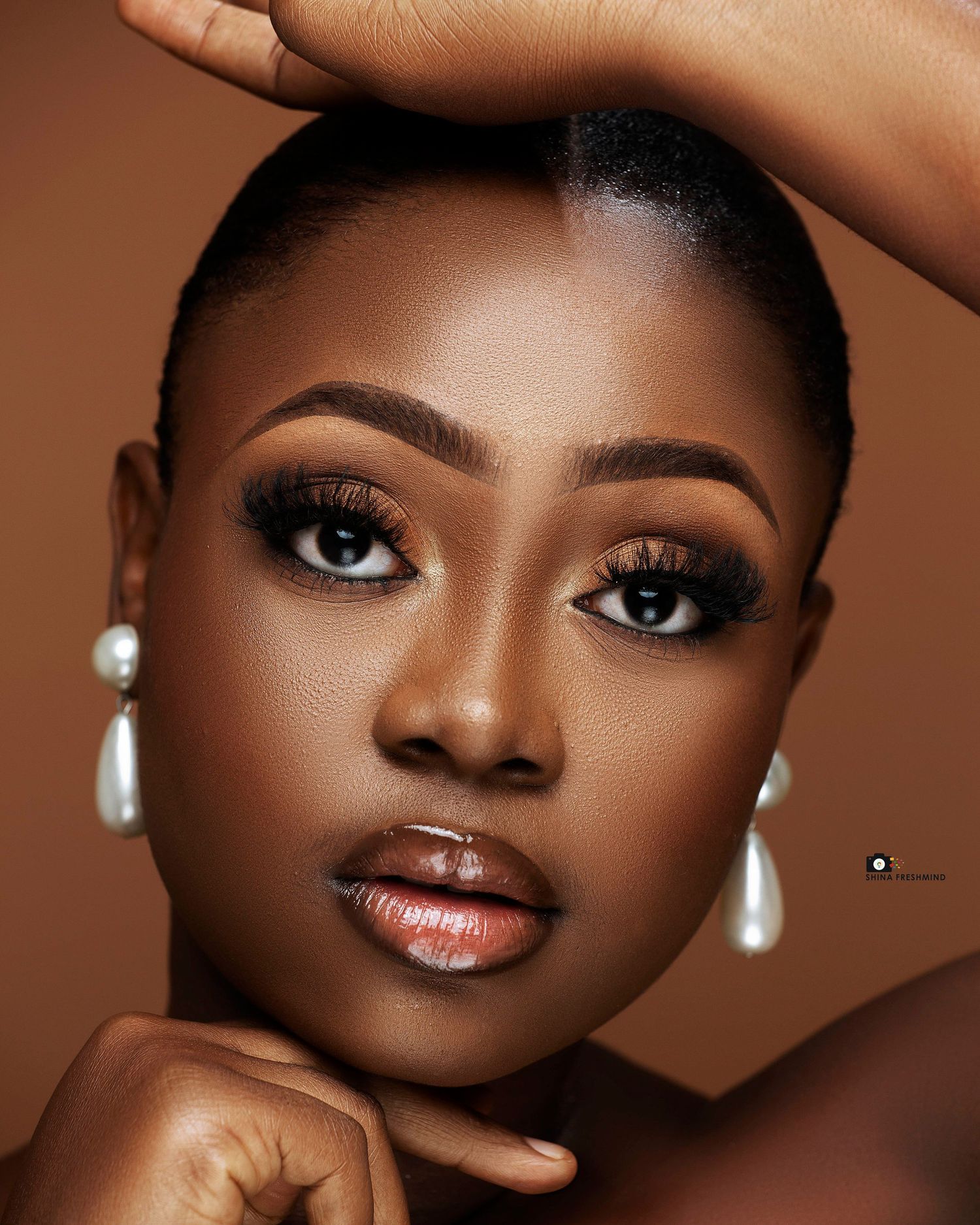 Close-up beauty portrait with smokey eye makeup and pearl earrings on brown background.