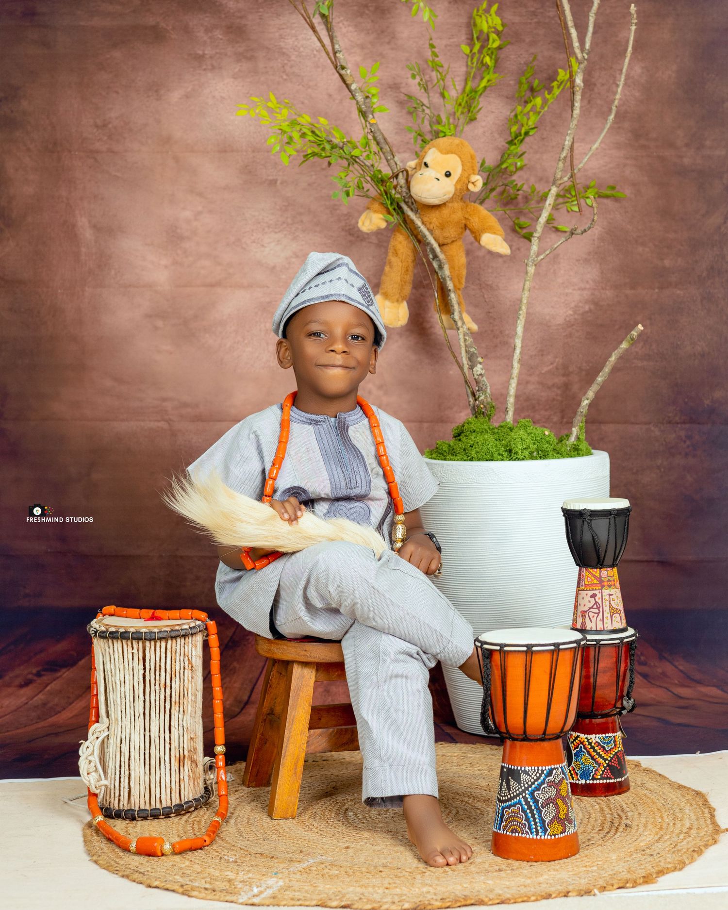 Child sitting with traditional African drums and musical instruments on woven mat.