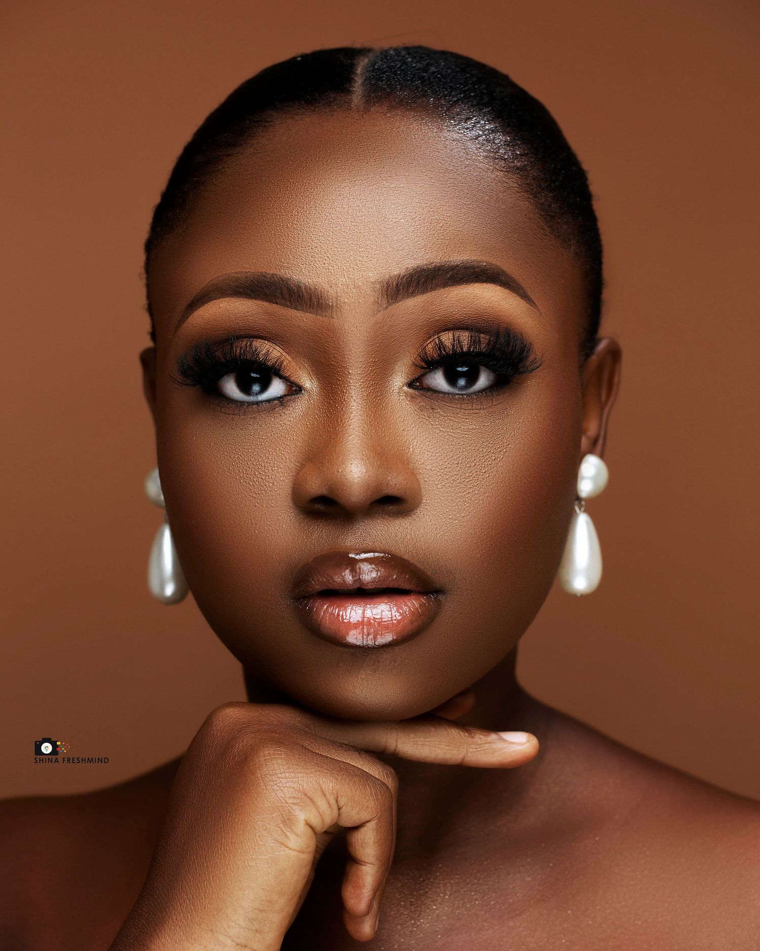 Elegant beauty portrait with pearl earrings and bronze makeup against brown background.