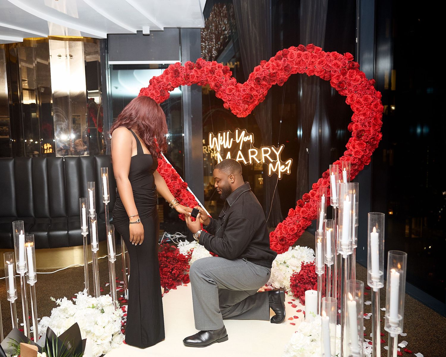 Proposal scene with red rose heart arch and candles creating romantic ambiance.