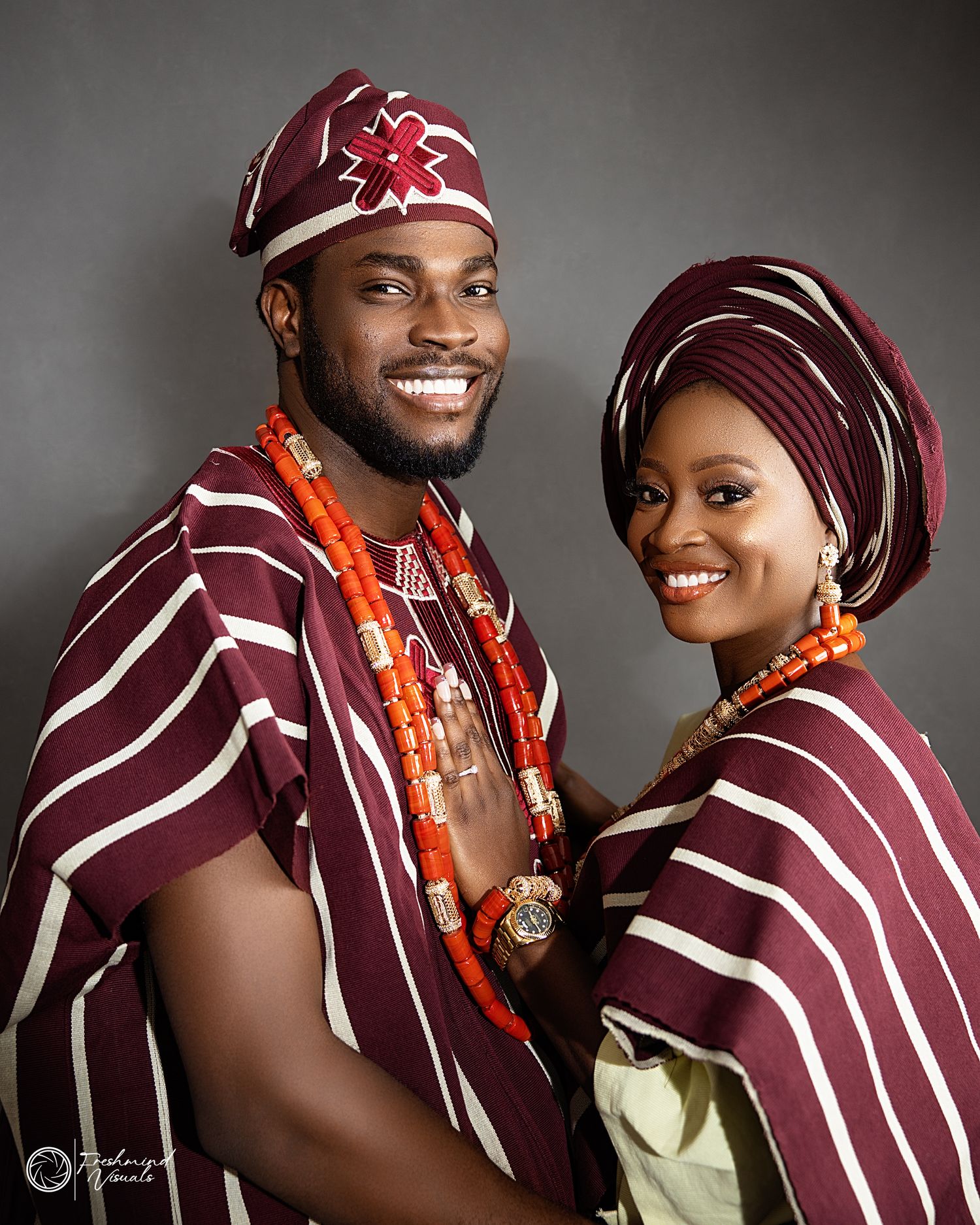 Couple in burgundy striped traditional attire sharing joyful moments during photo session.