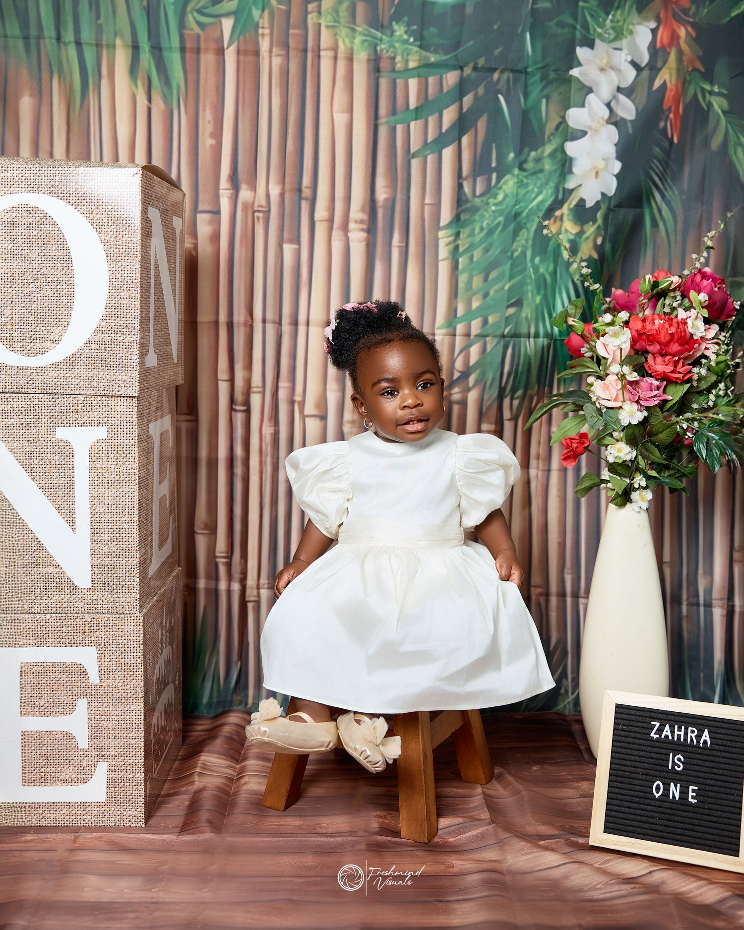 A series of first birthday photos featuring a white dress against a bamboo backdrop with floral decorations.