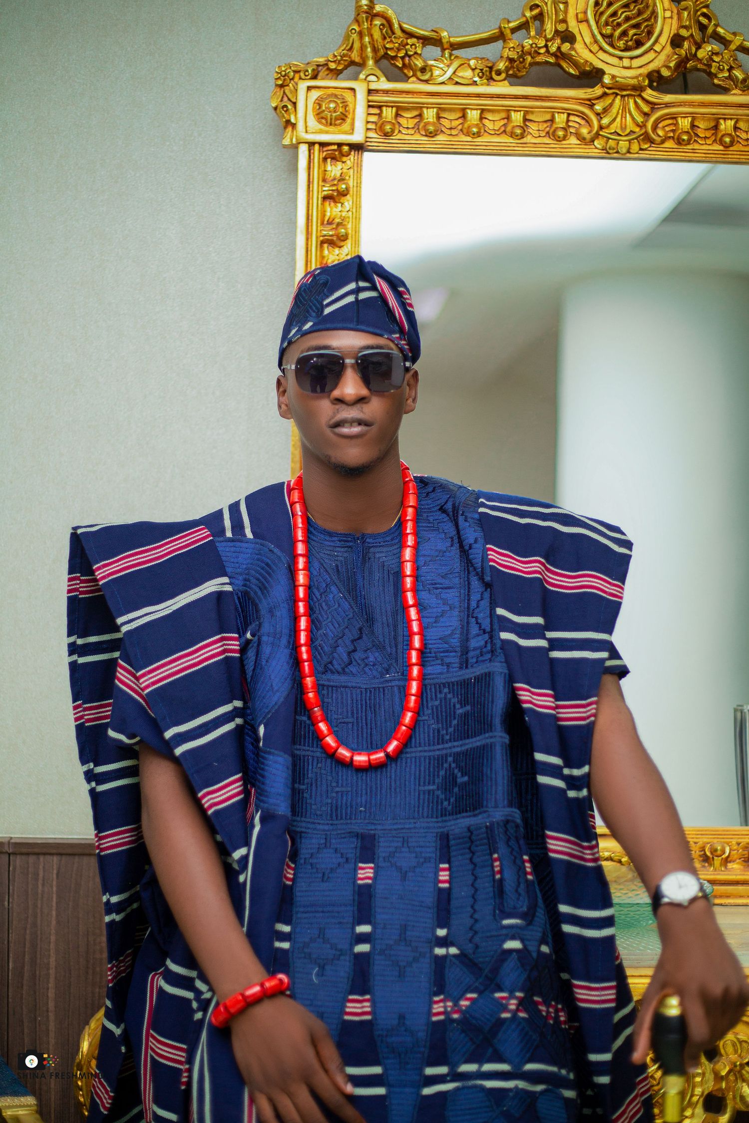 Traditional Nigerian attire featuring navy blue agbada with red beaded necklace and decorative stripes.