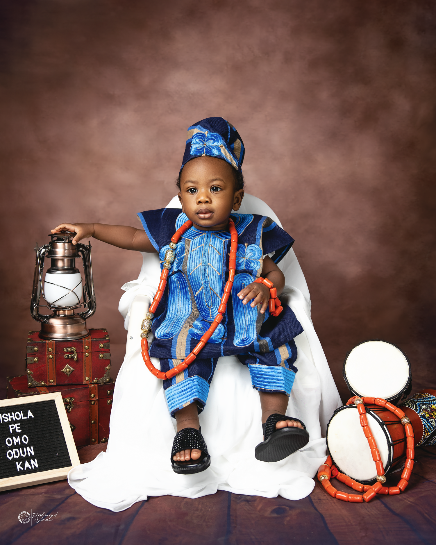 Studio portrait of toddler in traditional blue African attire with lantern and decorative props.