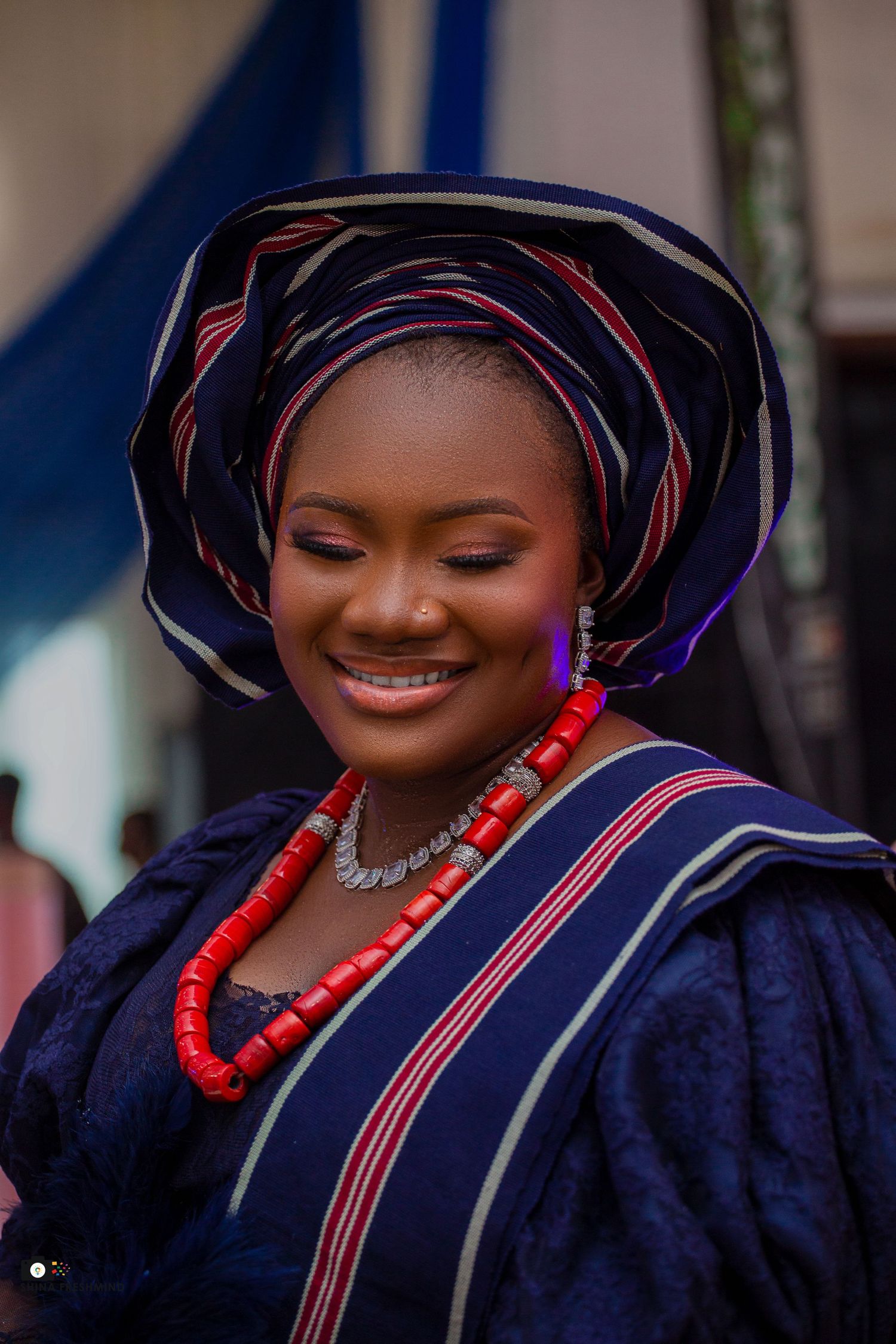 Traditional Nigerian attire featuring navy gele headwrap and red coral beaded necklace in portrait series.
