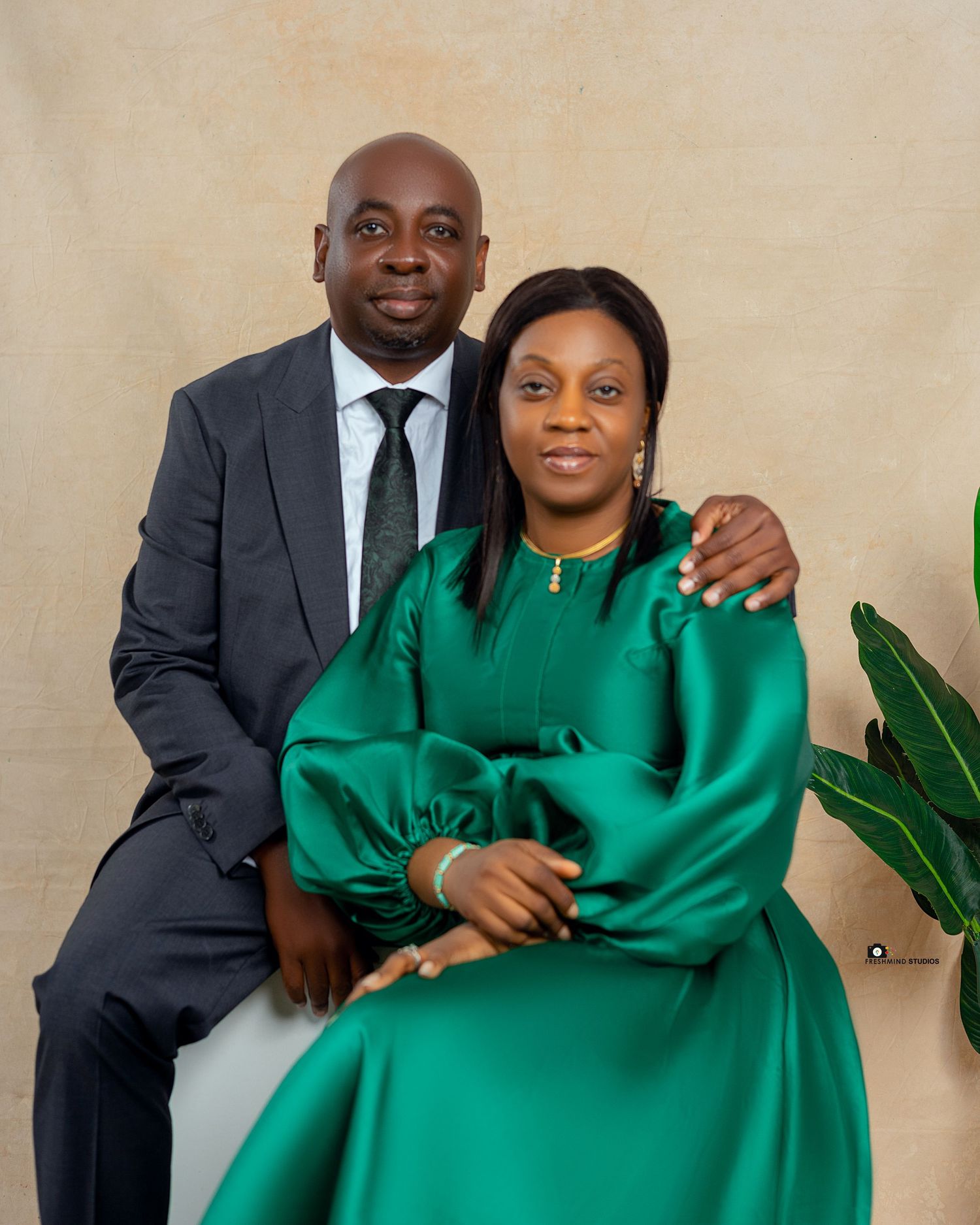 A couple poses together in formal attire, with one wearing a dark suit and the other in an emerald green dress.