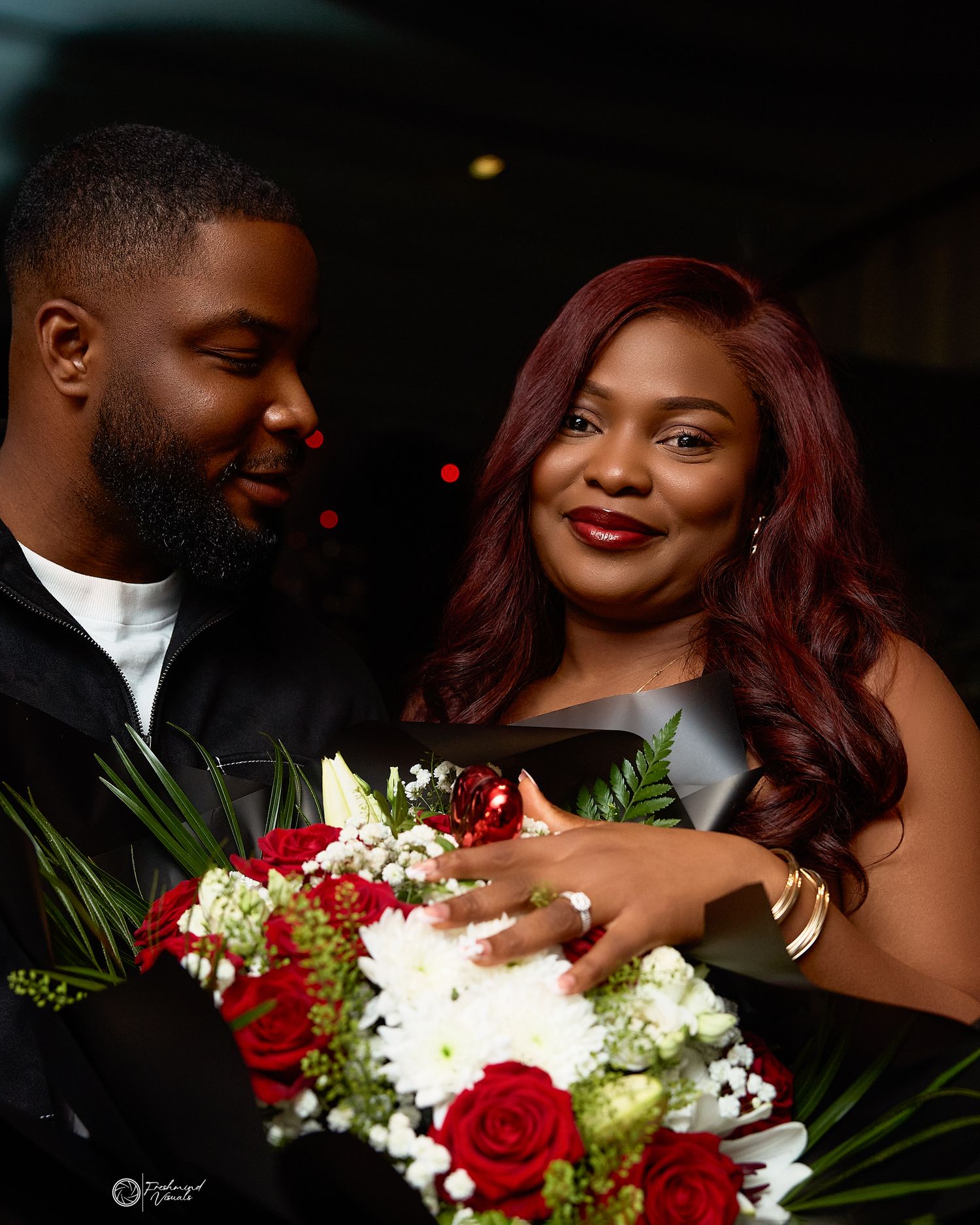 Romantic engagement photo with red and white floral bouquet.